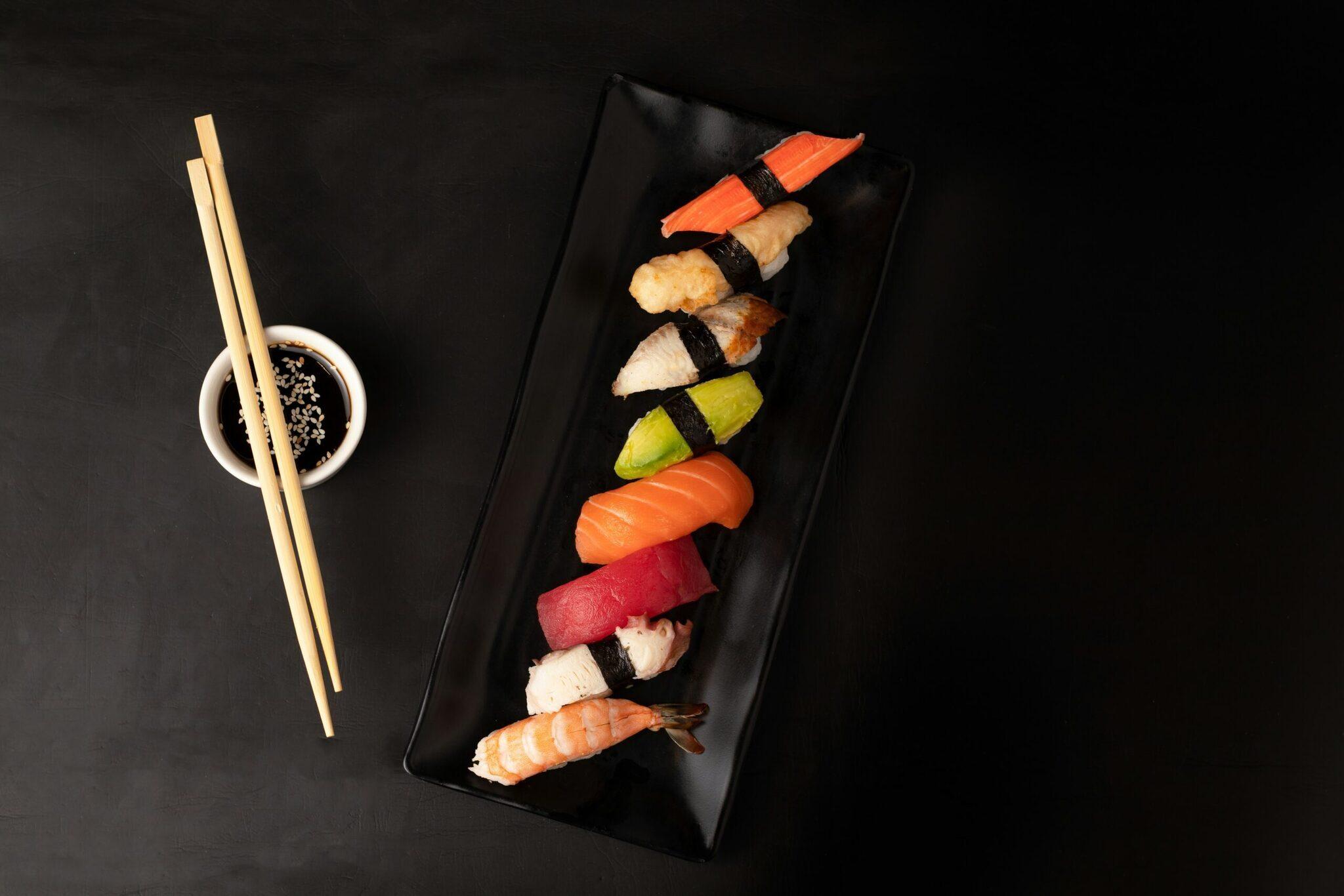 Assortiment de nigiri sushi variés présenté sur un plateau noir avec baguettes et sauce soja