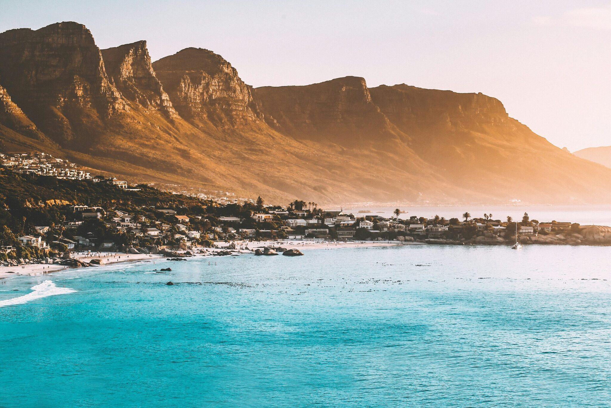 Une plage de sable blanc avec des eaux turquoise face à des montagnes rocheuses escarpées et une ville côtière