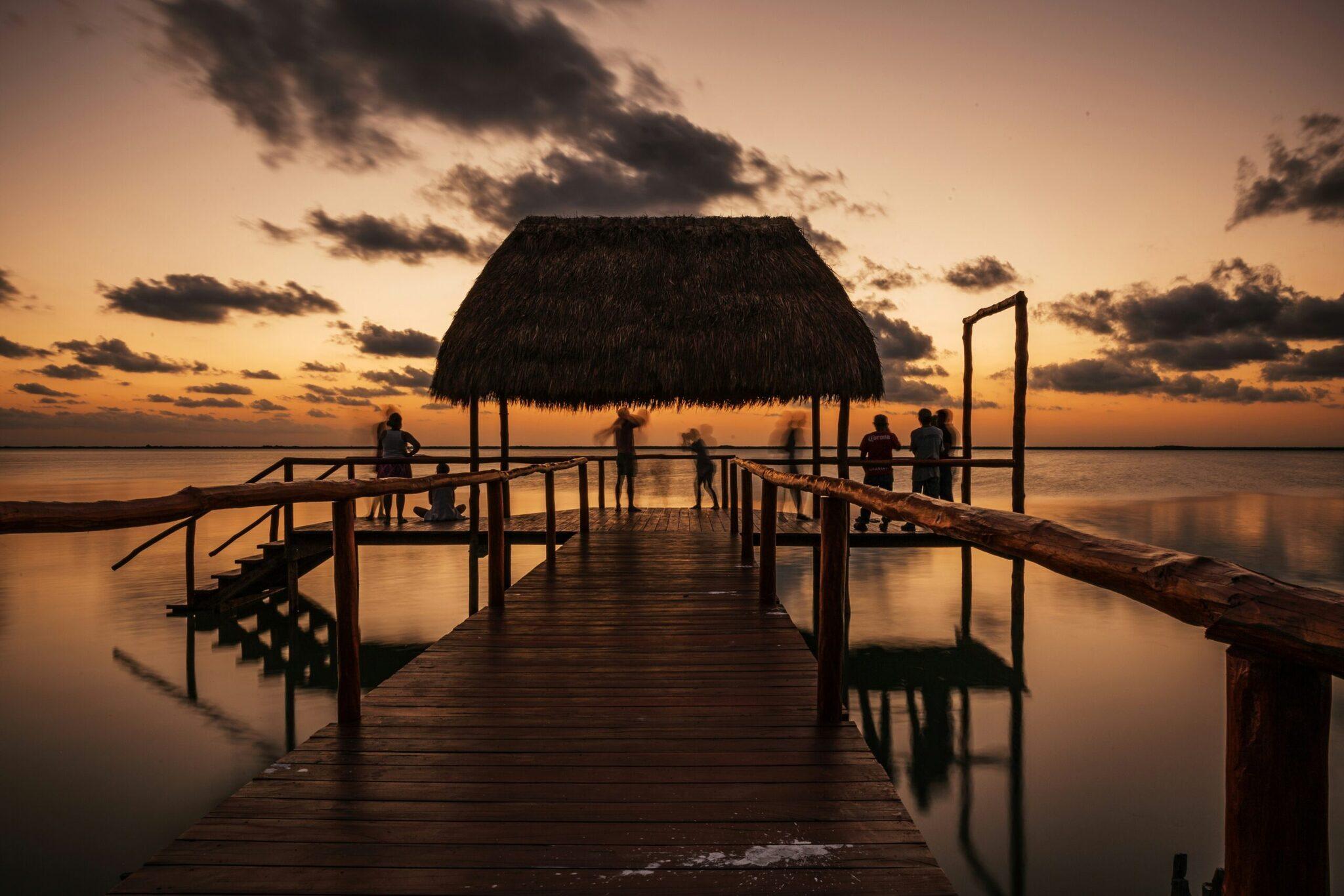 Un pontile in legno con un riparo dal tetto di paglia che conduce verso una baia tranquilla al tramonto
