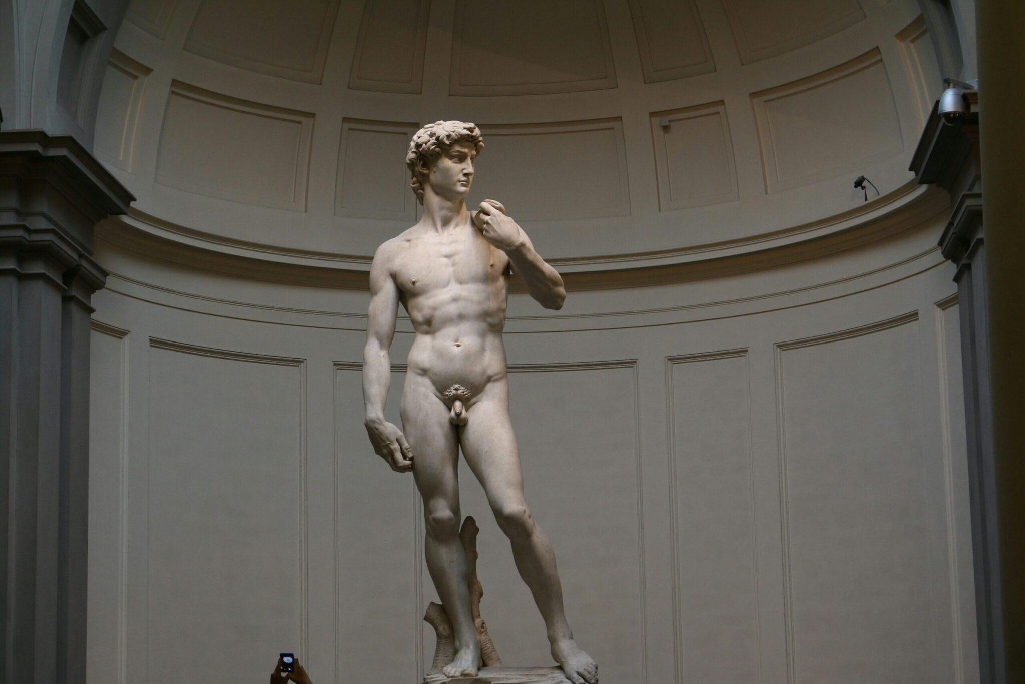 Statue en marbre blanc d’un jeune homme nu dans une galerie aux murs épais et plafond dôme