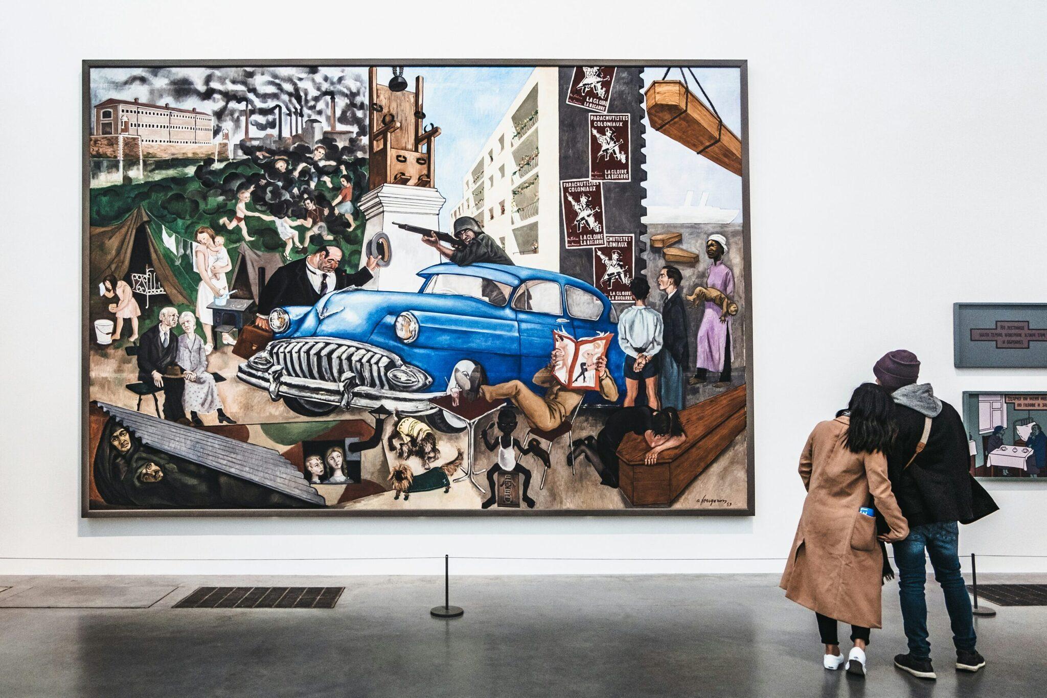 Zwei Besucher betrachten ein farbenfrohes Wandbild mit einem Oldtimer-Auto und Stadtszenen in einem Museum