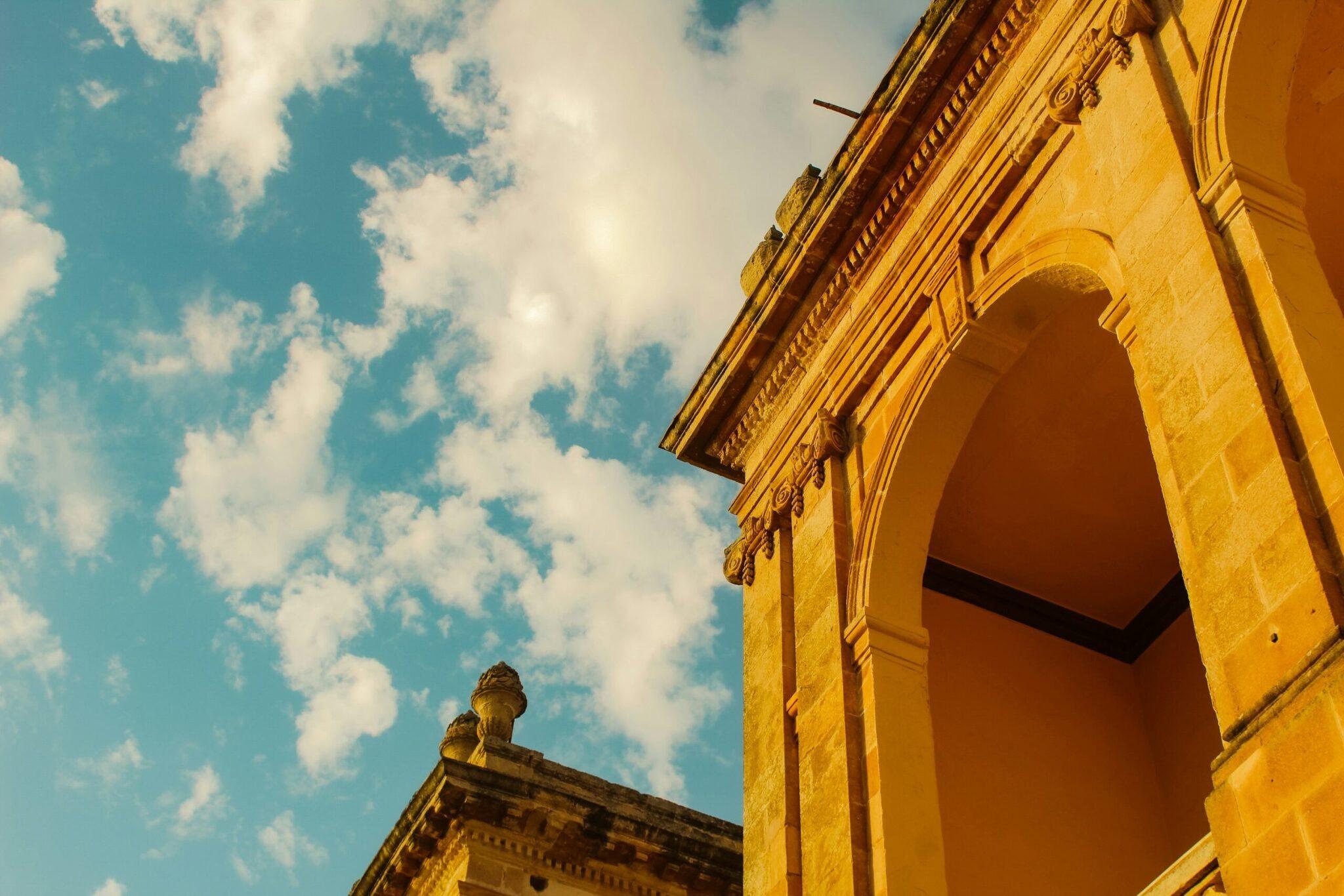 Arco de piedra amarilla de un edificio histórico bajo cielo azul con nubes blancas