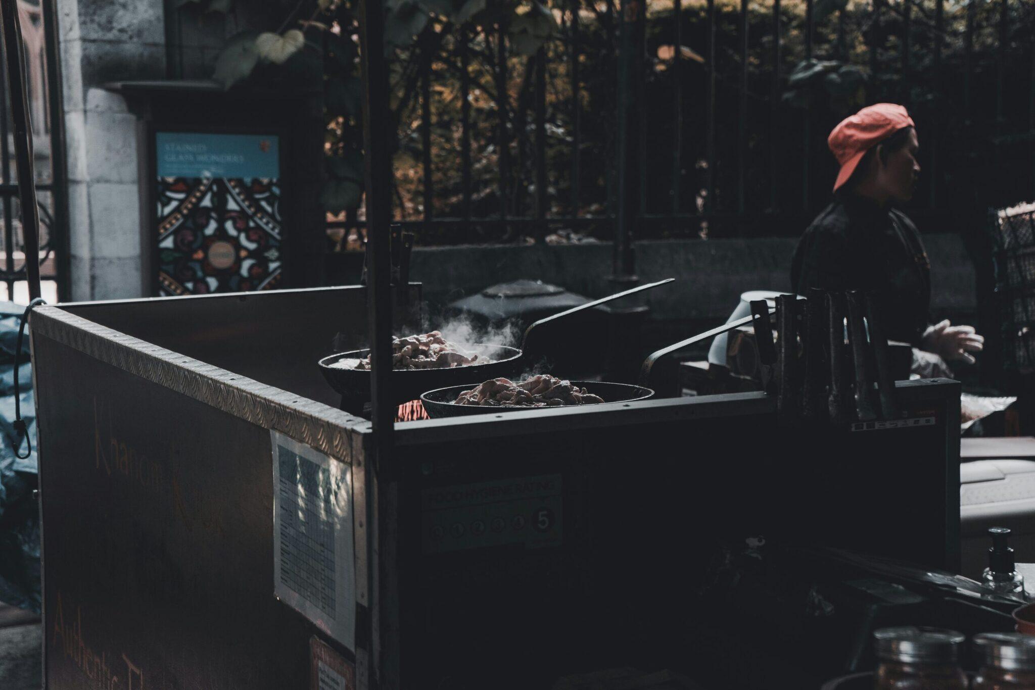 Ein Street-Food-Verkäufer bereitet Gerichte in Woks in einer belebten asiatischen Stadtgasse zu