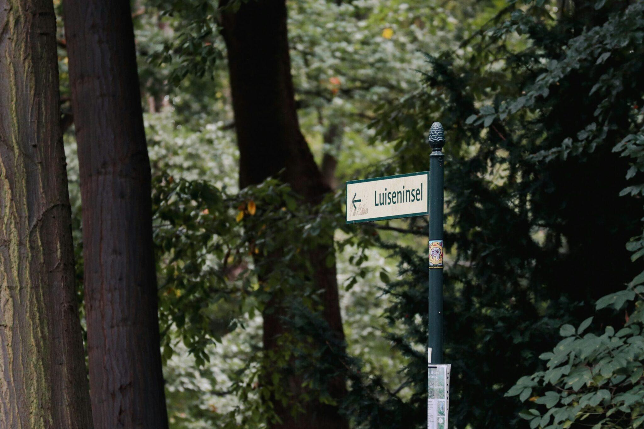 A “Luiseninsel” street sign in a leafy lane flanked by old brick walls and trees