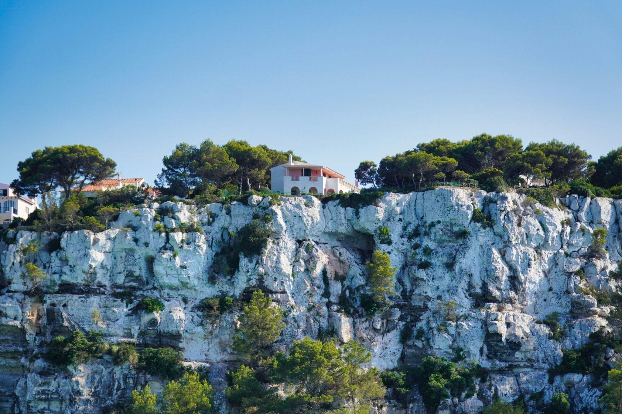 Casa mediterránea blanca encaramada en un escarpado acantilado calizo rodeada de vegetación