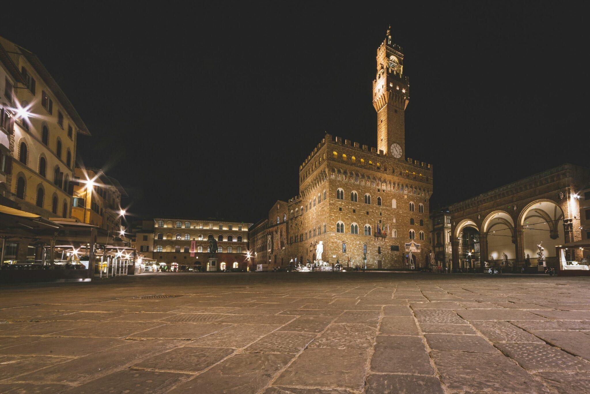 Place historique italienne de nuit illuminée avec un palais médiéval surmonté d’une tour horloge