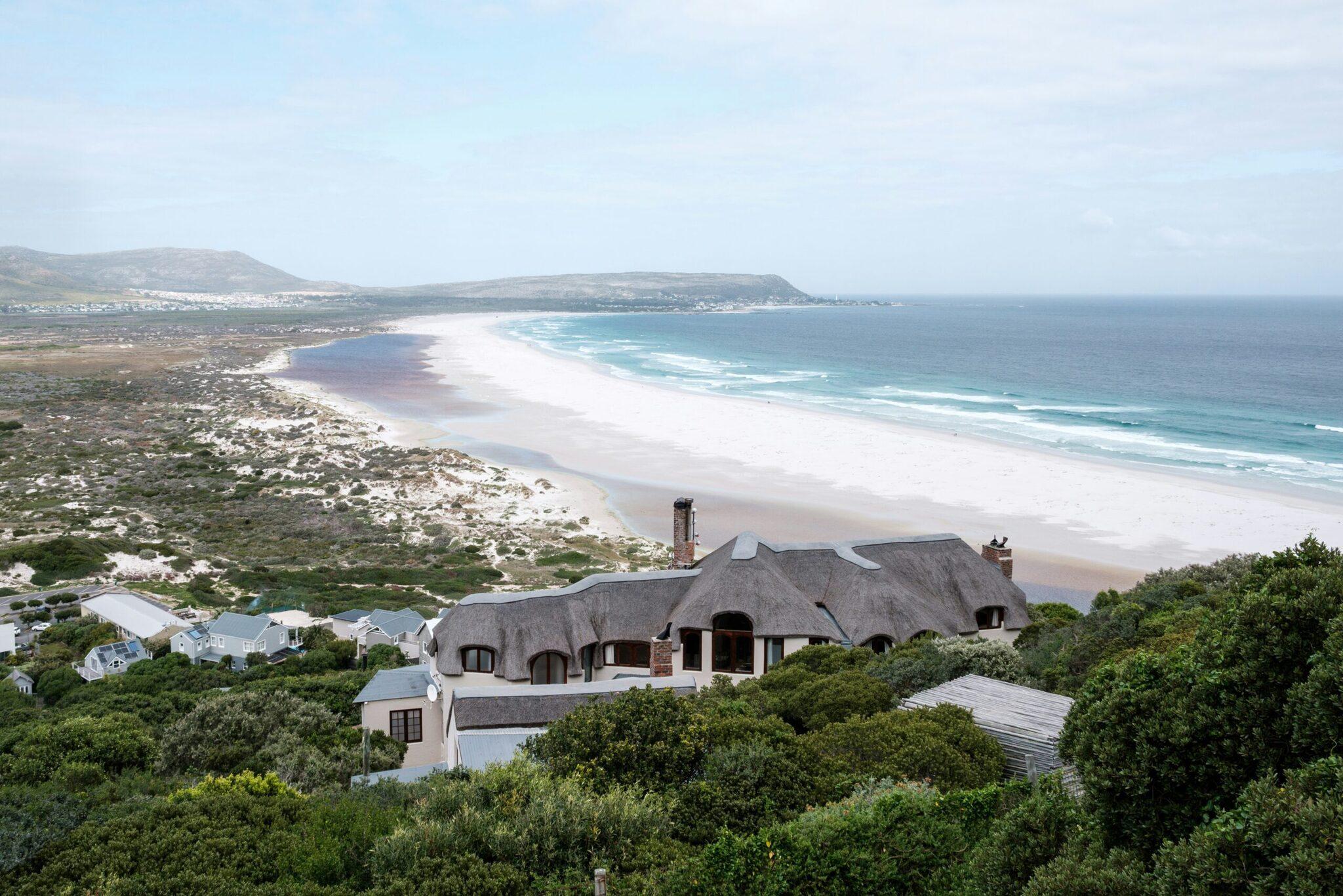 Maison moderne au toit de chaume surplombant une vaste plage de sable blanc et l’océan turquoise en Afrique du Sud