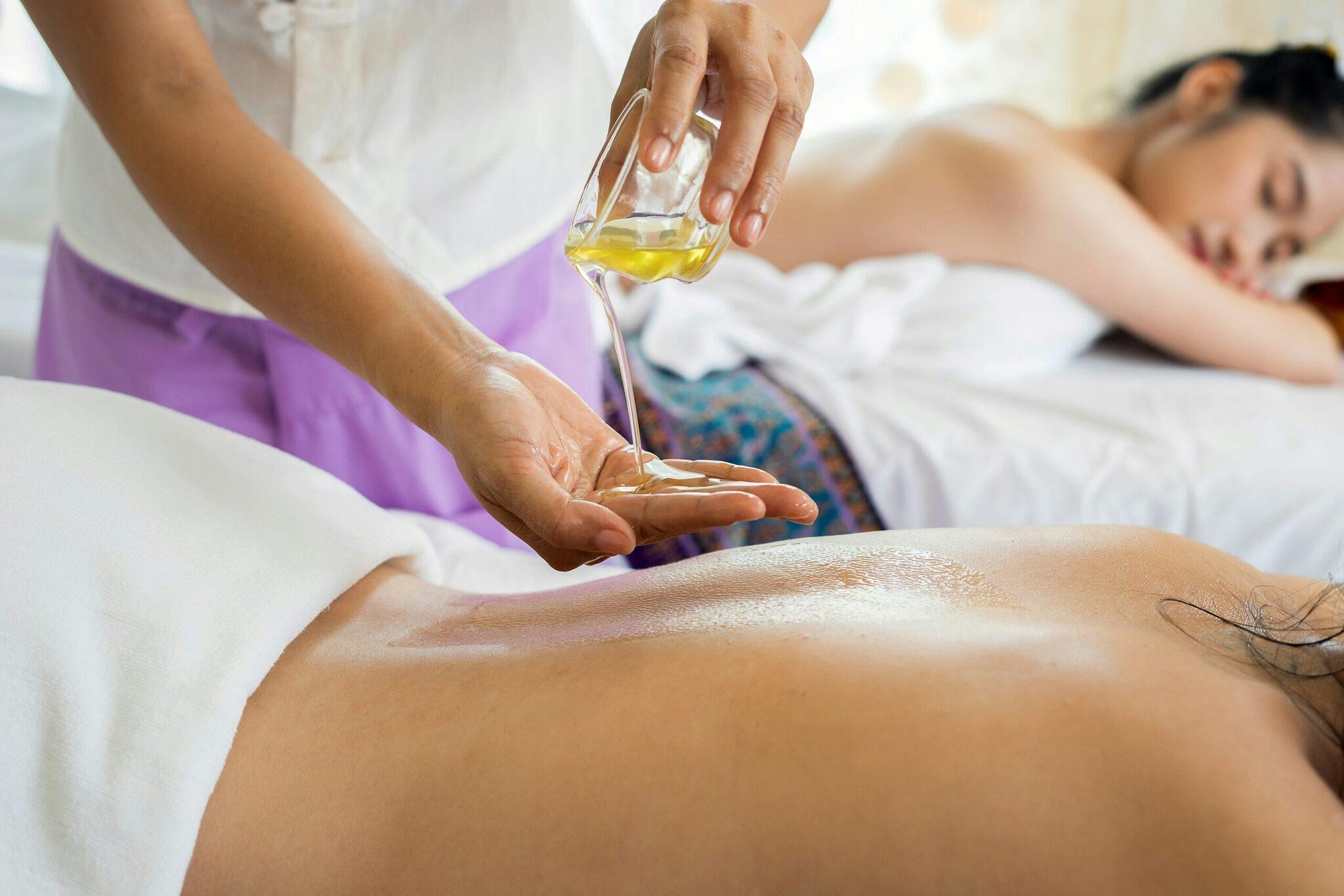 Une thérapeute verse de l’huile de massage sur le dos d’une cliente allongée dans un spa
