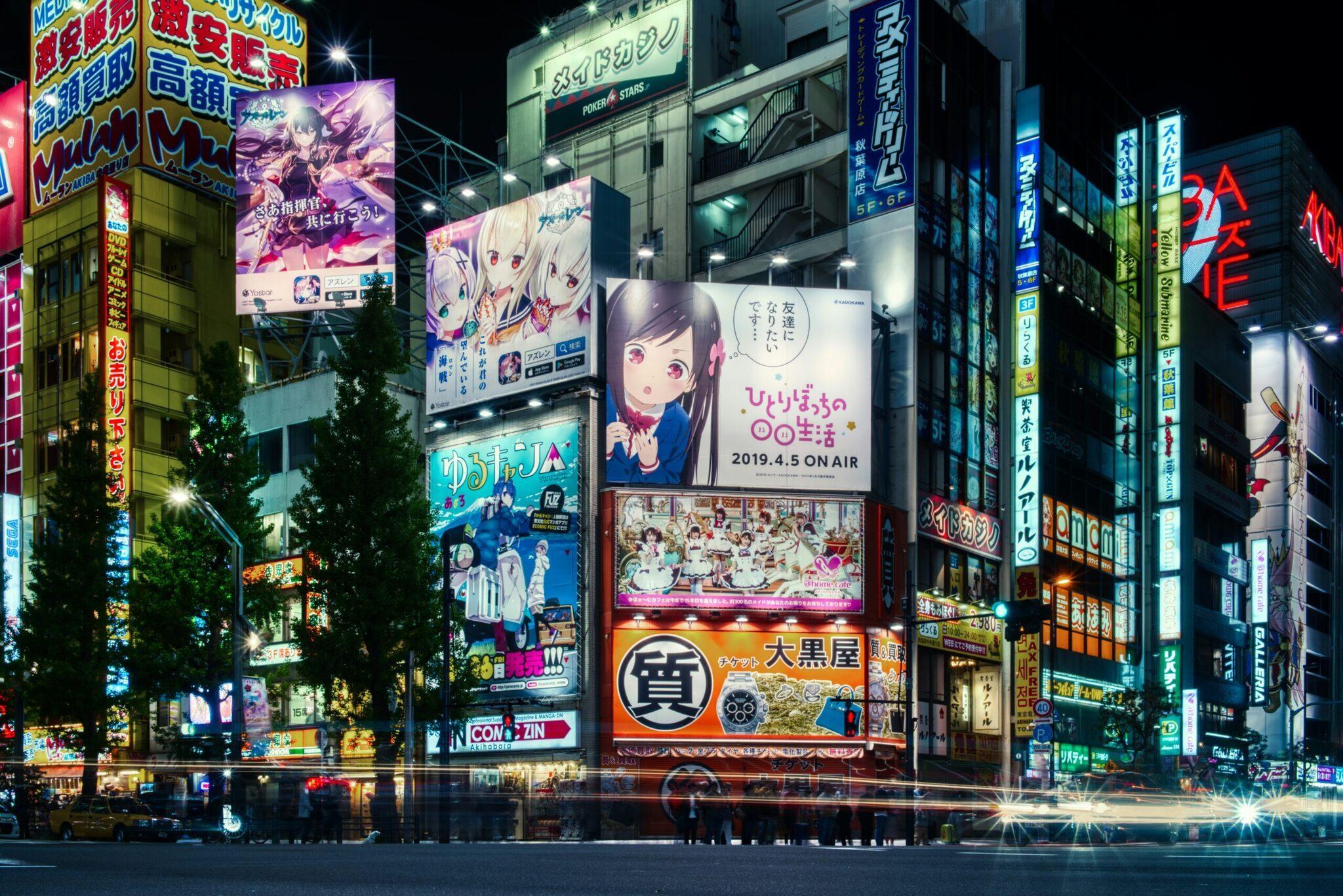 Une rue commerçante animée de nuit avec immeubles illuminés, panneaux publicitaires colorés et affiches d’anime japonais