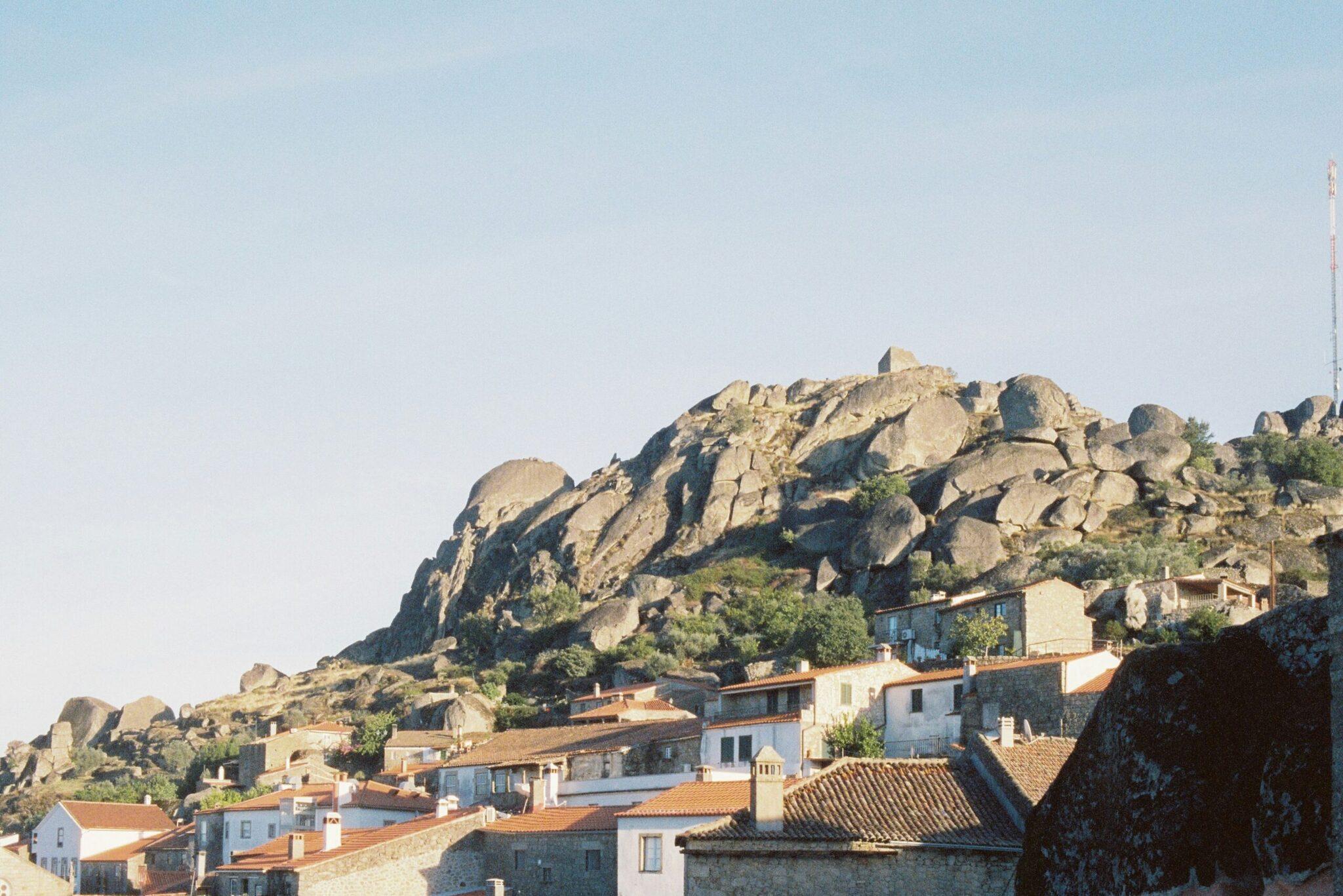A village of white houses and red-tiled roofs built into a rocky mountain scattered with giant boulders