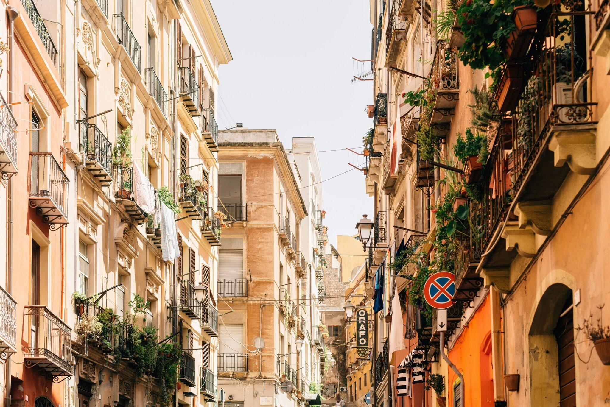 Une ruelle étroite méditerranéenne avec façades colorées, balcons ornés, végétation grimpante et panneaux de circulation