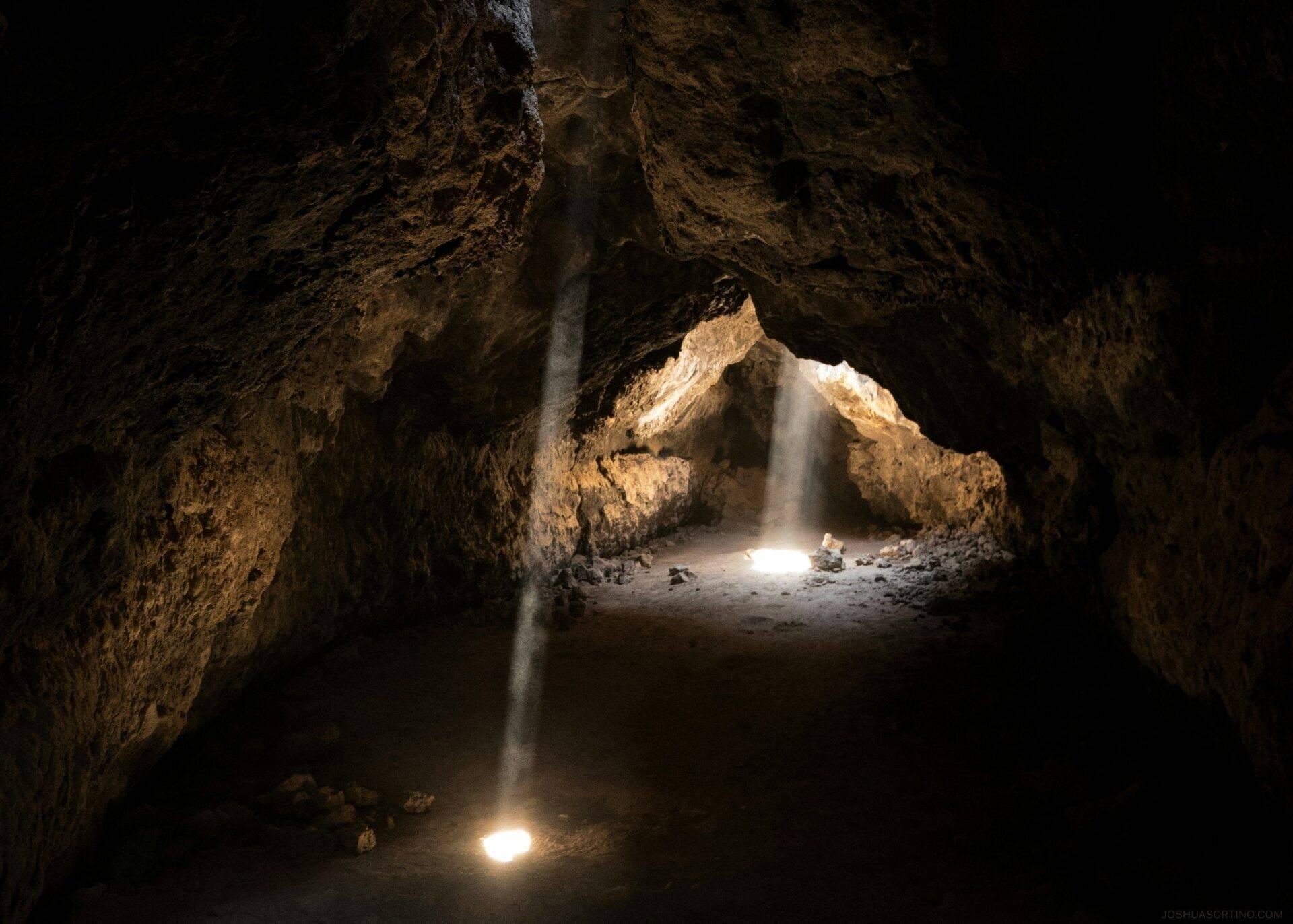 Interno di una grotta calcarea con raggi di luce che attraversano l’oscurità e vista sull’ingresso illuminato