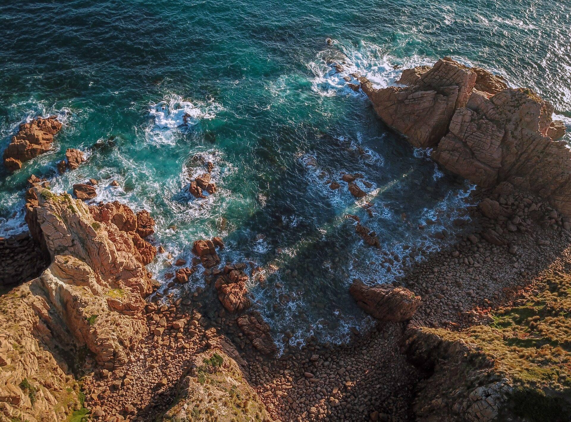 Vista aérea de una costa rocosa con acantilados rojos, olas turquesas y espectaculares formaciones geológicas
