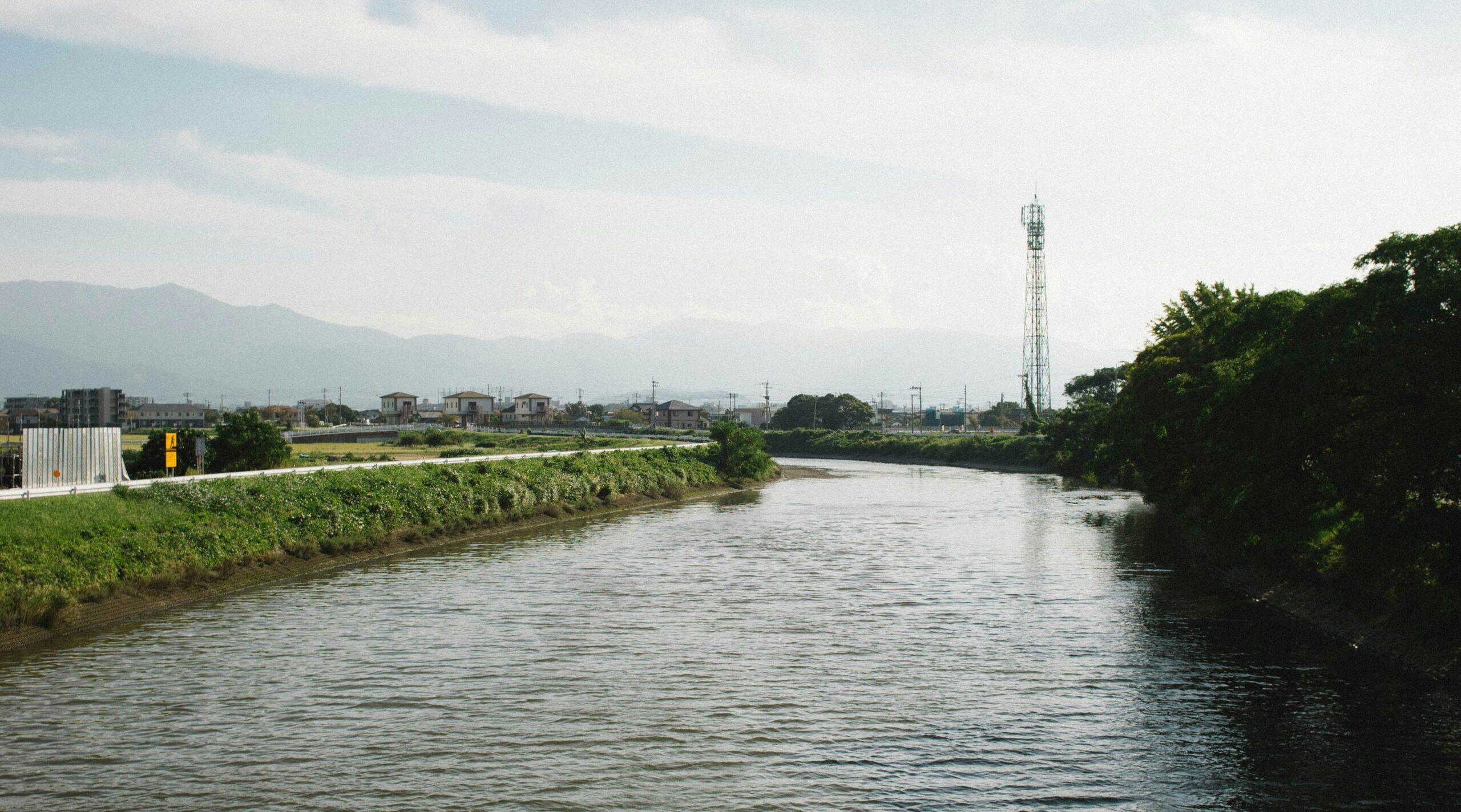 Vue d’une rivière traversant une zone rurale japonaise avec maisons traditionnelles et tour de communication en arrière-plan