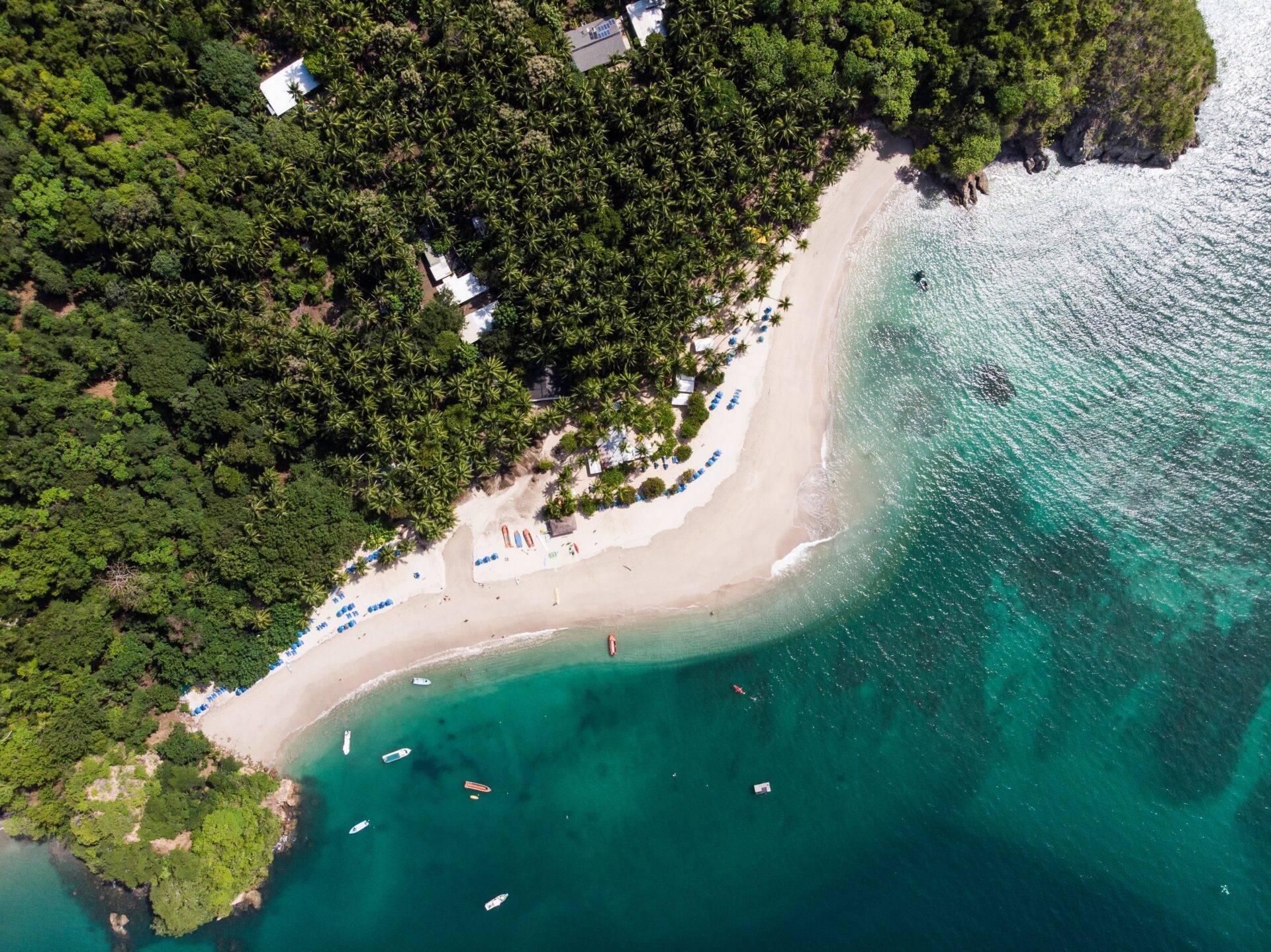 Vue aérienne d’une plage de sable blanc bordée de forêt tropicale avec bateaux ancrés dans une eau turquoise cristalline