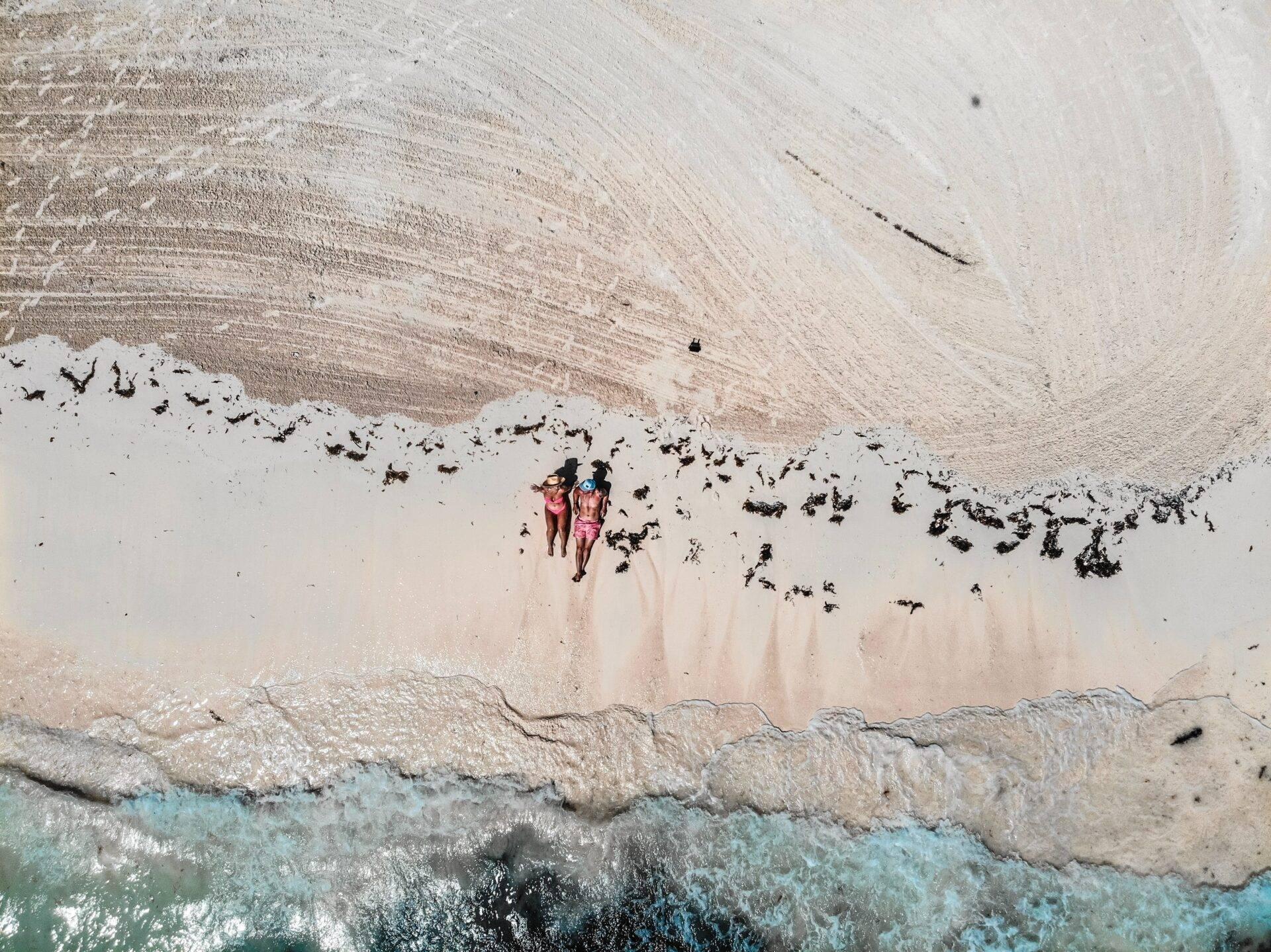 Dos personas en bañador en una playa de arena blanca frente a olas turquesas cristalinas