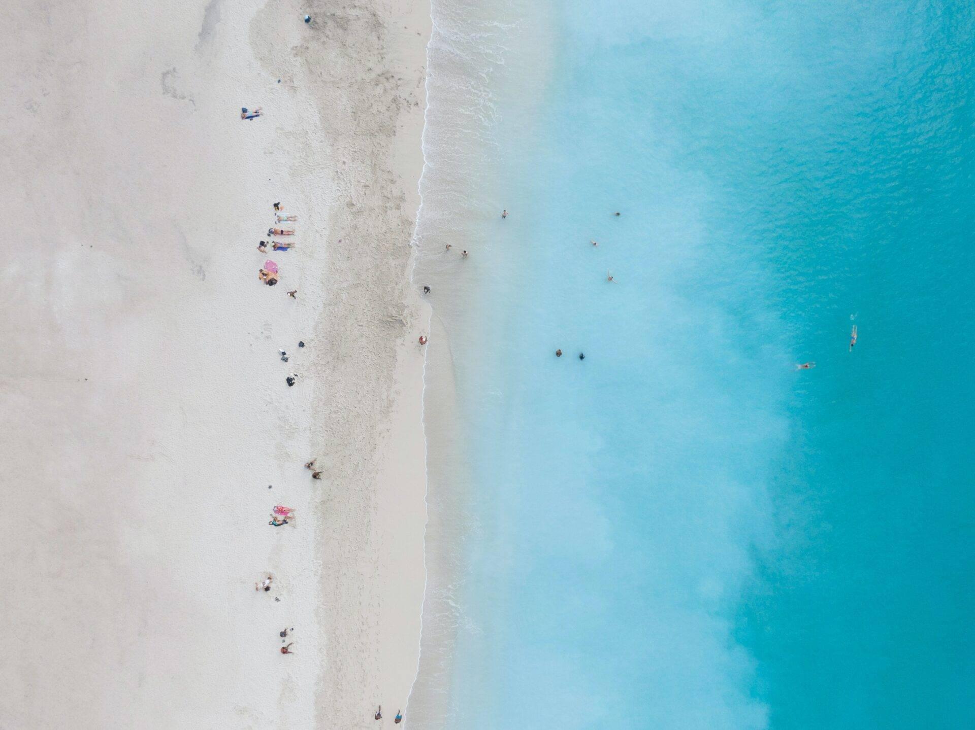 Aerial view of a white sand beach with scattered swimmers and crystal-clear turquoise waters
