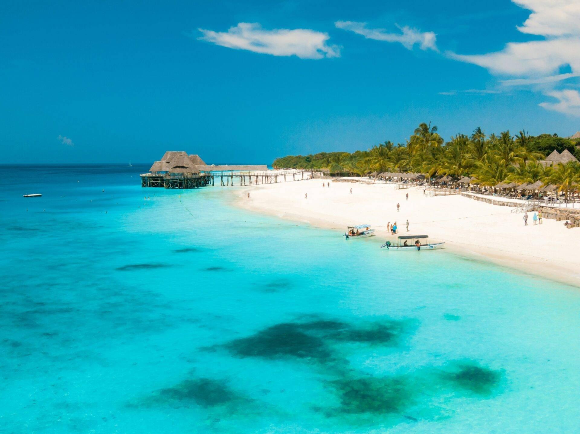 Plage tropicale avec lagon turquoise, bungalow sur pilotis, palmiers et sable blanc sous ciel bleu