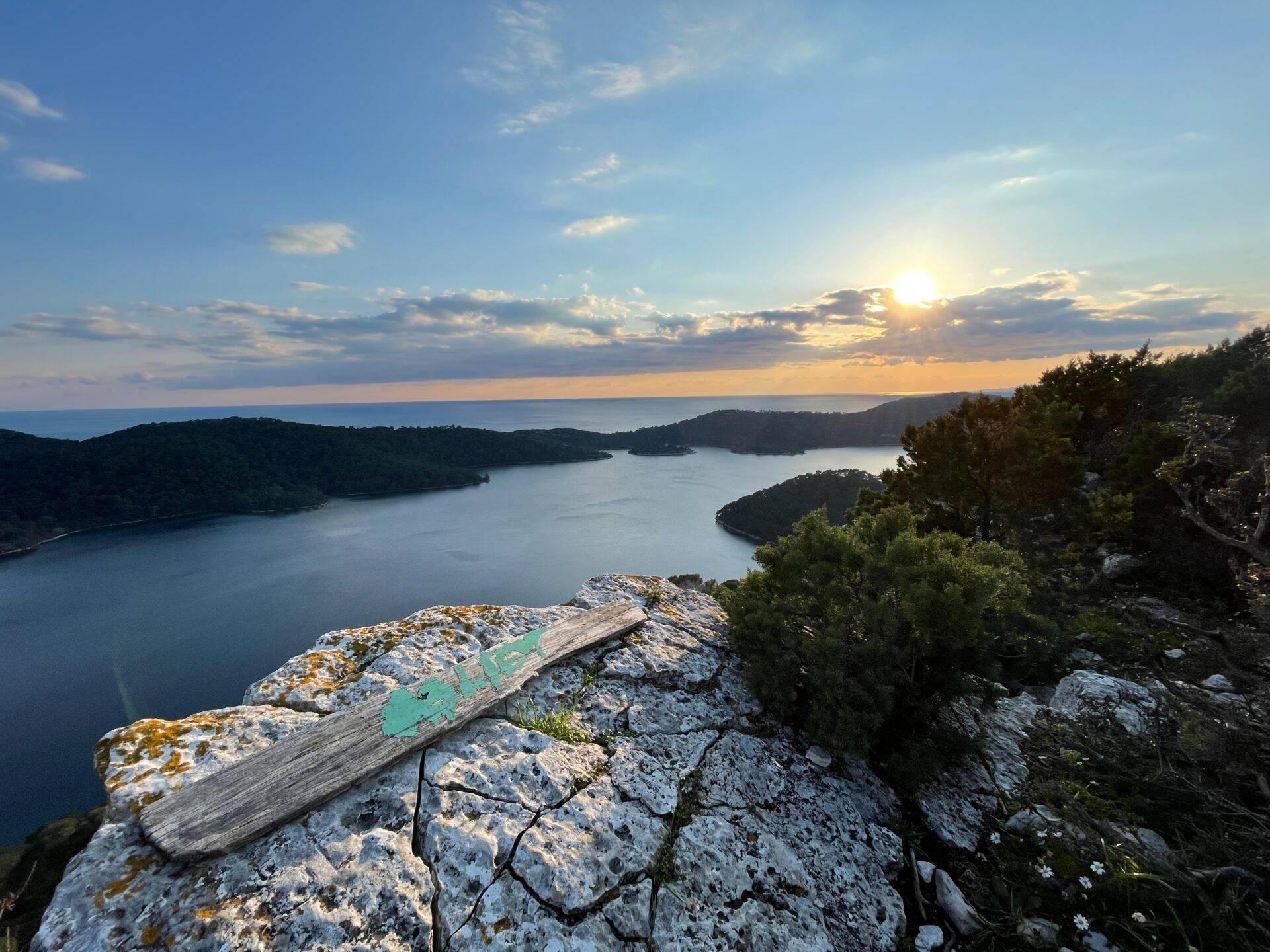 Panoramaansicht bei Sonnenuntergang über eine mediterrane Küste mit bewaldeten Buchten und Felsklippen