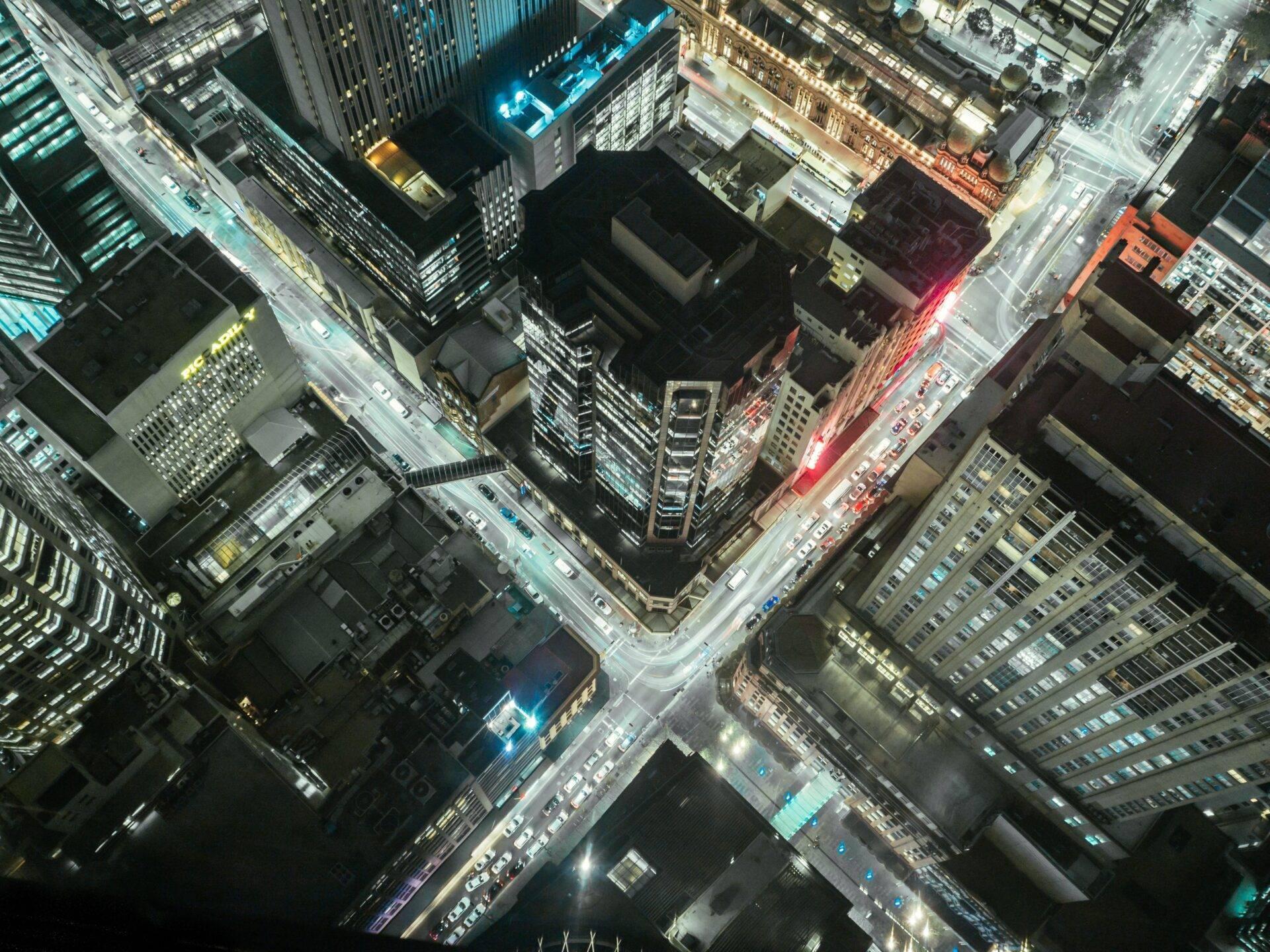 Vista aérea nocturna de una concurrida intersección urbana con edificios iluminados y tráfico rodado