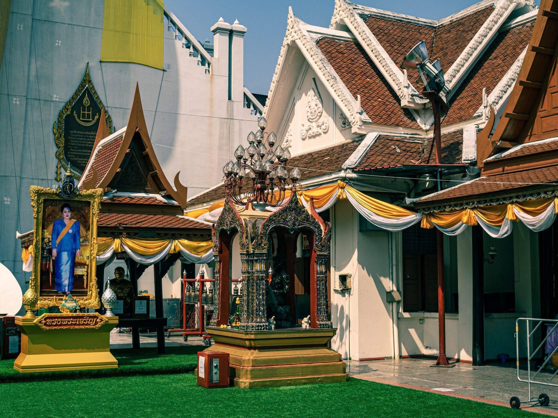 Un temple bouddhiste thaïlandais avec toits dorés, décorés de drapeaux jaunes et blancs, sous un ciel bleu ensoleillé