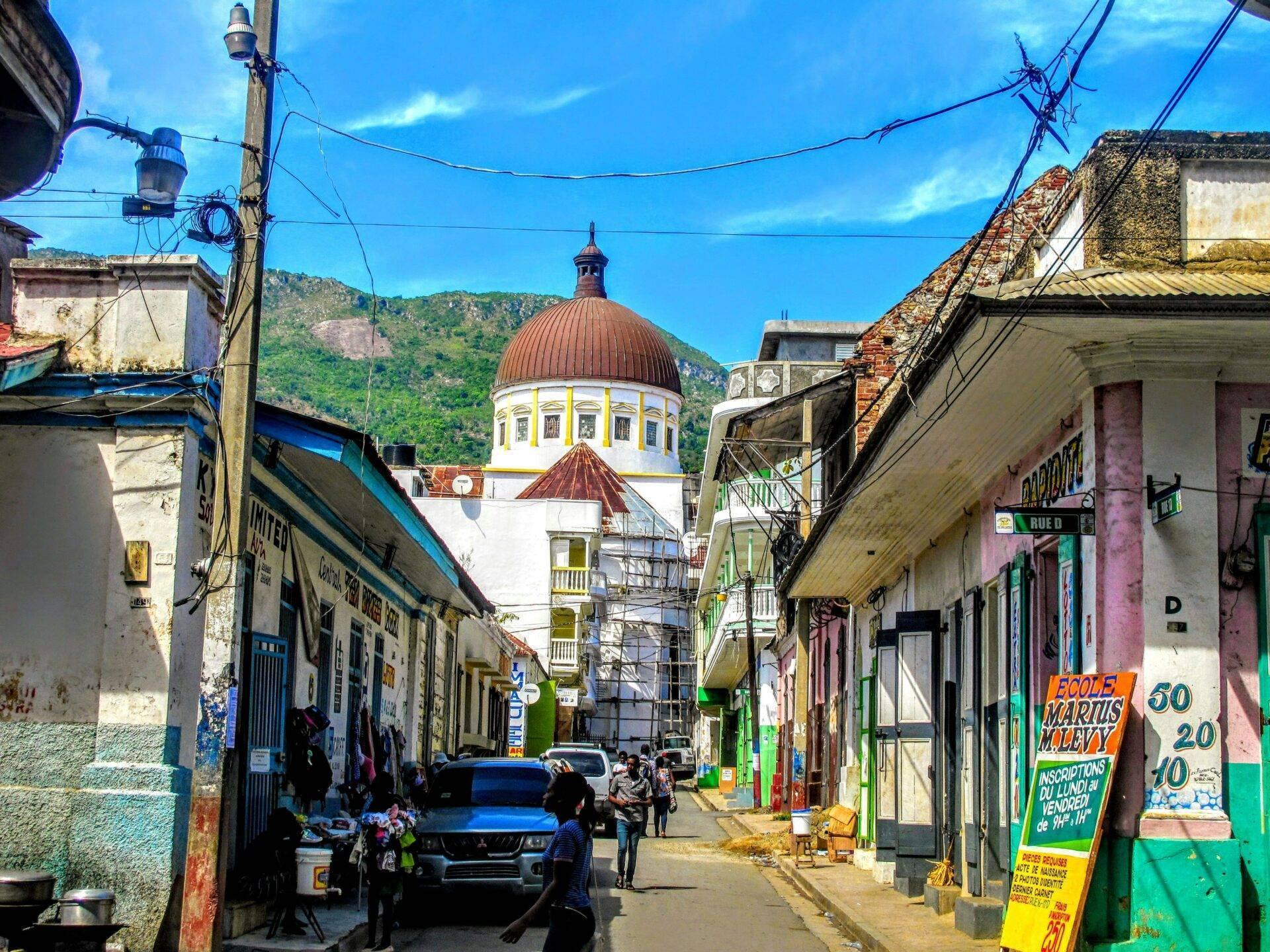 Una strada colorata di una città caraibica con una chiesa a cupola rossa che domina l’orizzonte montuoso