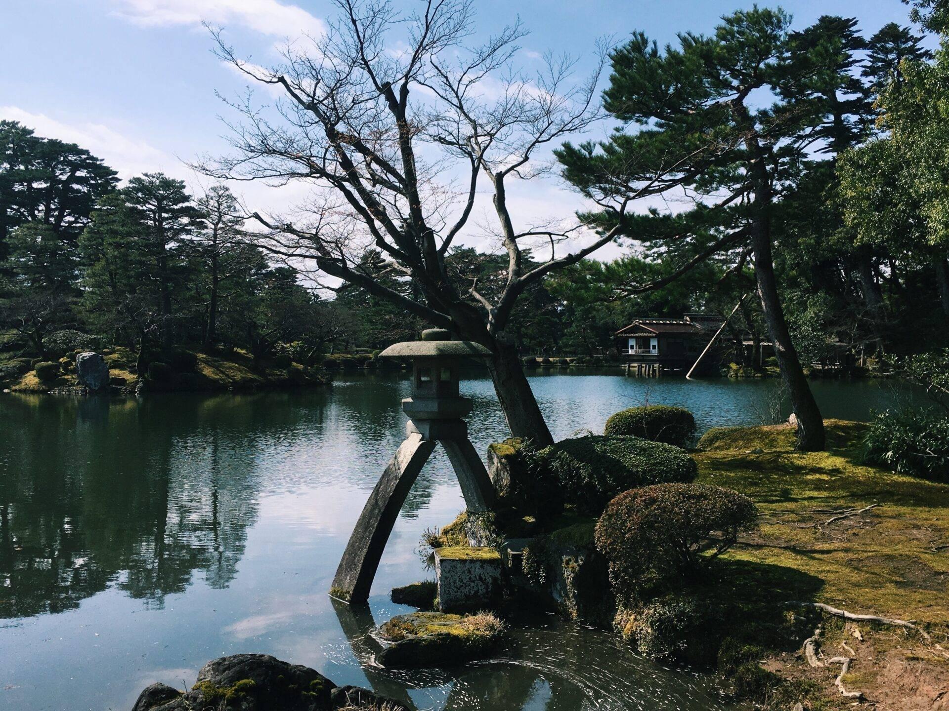 Un jardin japonais traditionnel avec un étang calme, des arbres anciens et une maison de thé au bord de l’eau