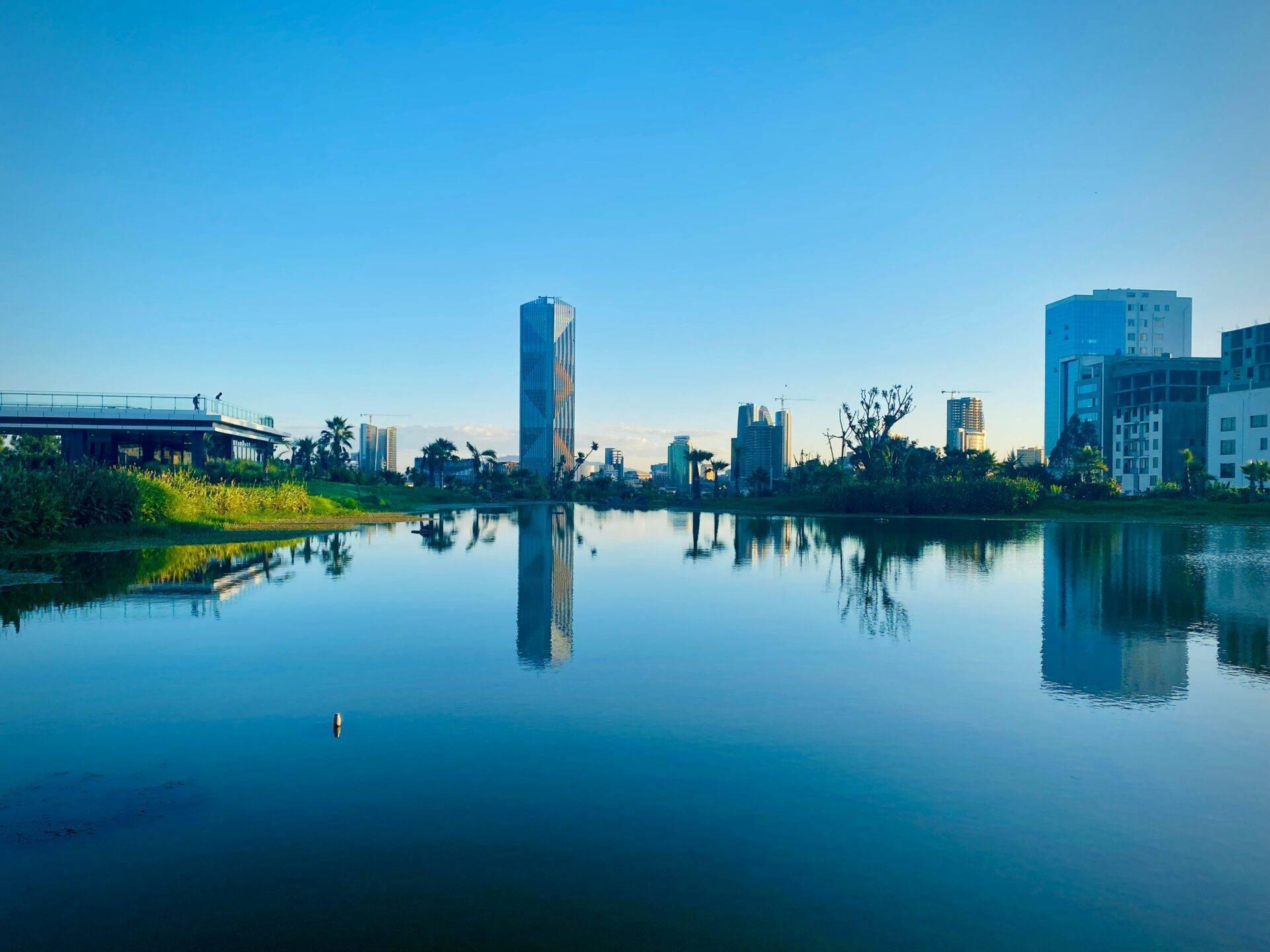 Moderne Stadtsilhouette, die sich in einem ruhigen Fluss spiegelt, mit Vegetation und Brücke