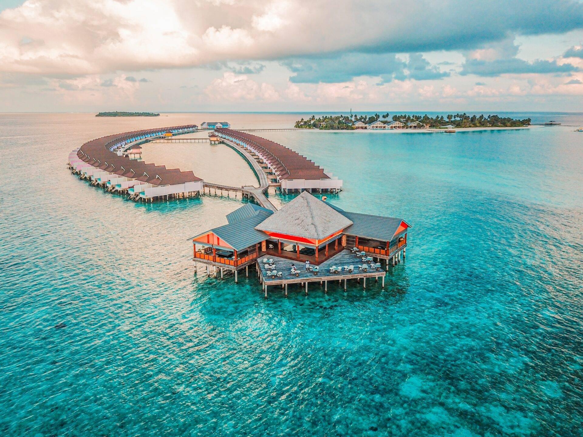 Vue aérienne d’un resort tropical aux bungalows sur pilotis en forme de spirale avec lagon turquoise et îles densément boisées