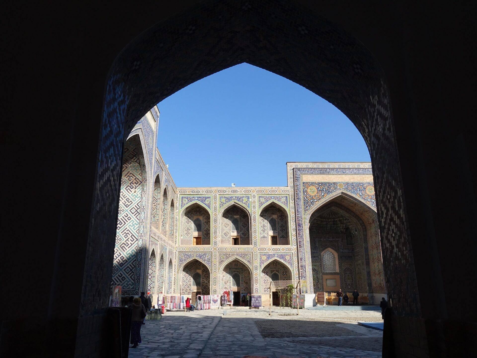 Vue depuis une arche d’entrée sur une cour intérieure ornée de mosaïques bleues et de motifs géométriques islamiques