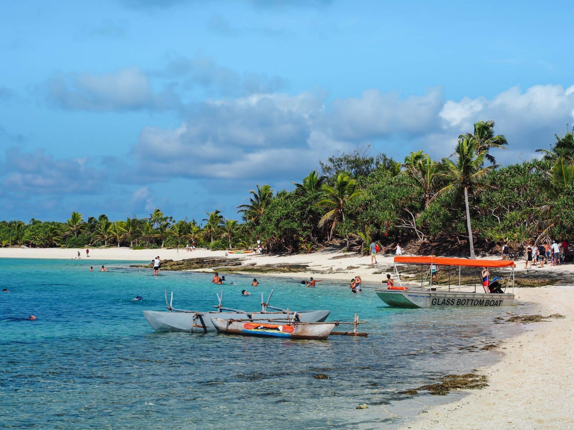 Plage tropicale avec bateaux de pêche traditionnels, baigneurs et palmiers sous ciel partiellement nuageux
