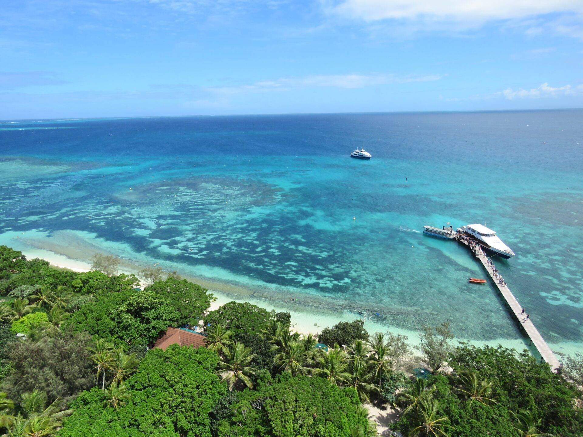 Vue aérienne d’une île tropicale avec plage de sable blanc, lagon turquoise et bateaux amarrés à un ponton