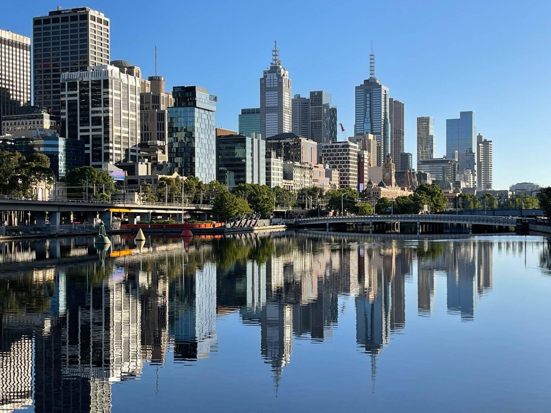 Skyline urbano moderno con rascacielos reflejados en las aguas tranquilas de un río, árboles y muelles en primer plano