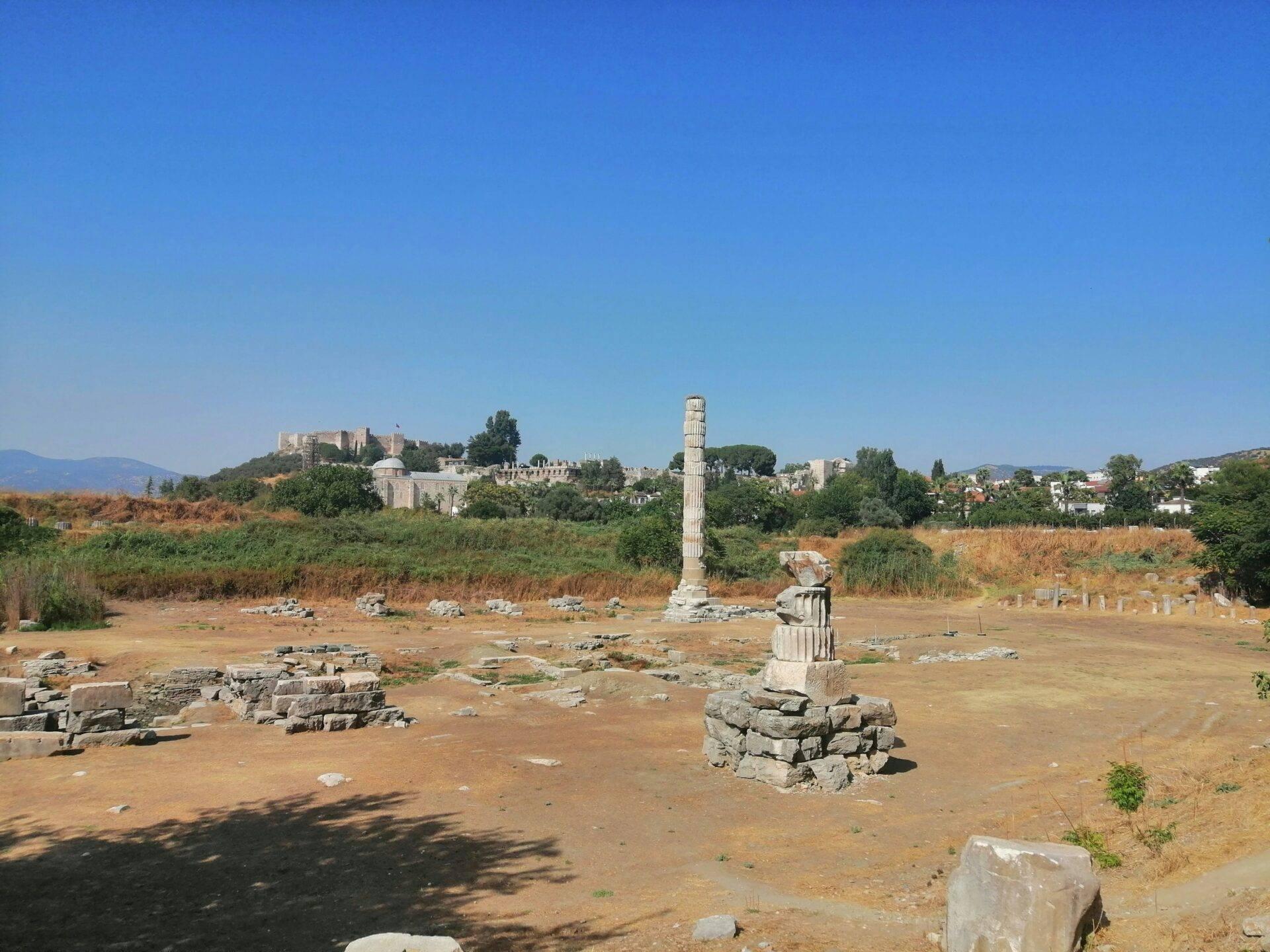 Ruines antiques avec colonne isolée, temple en arrière-plan et montagnes sous ciel dégagé