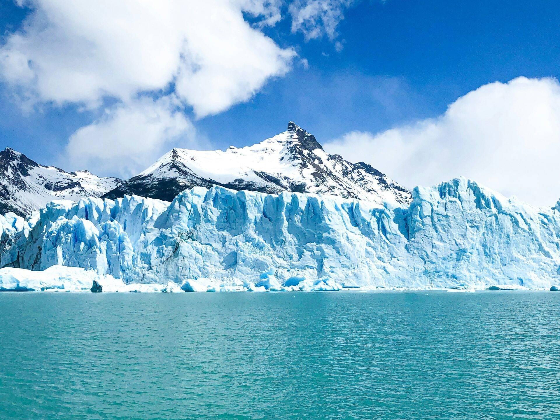 Un glacier bleu massif avec ses formations de glace caractéristiques face à une montagne enneigée sous ciel dégagé