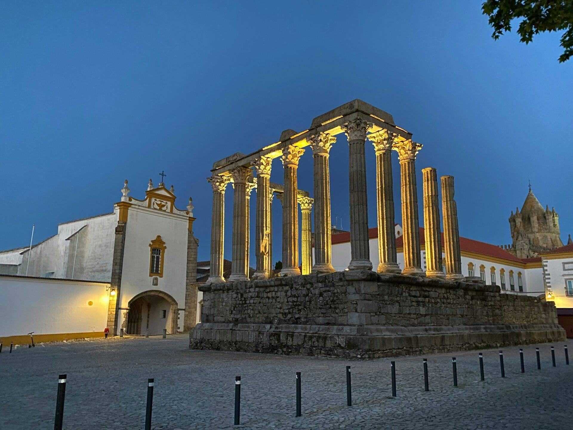 Rovine romane illuminate con colonne corinzie e chiese bianche sullo sfondo al crepuscolo