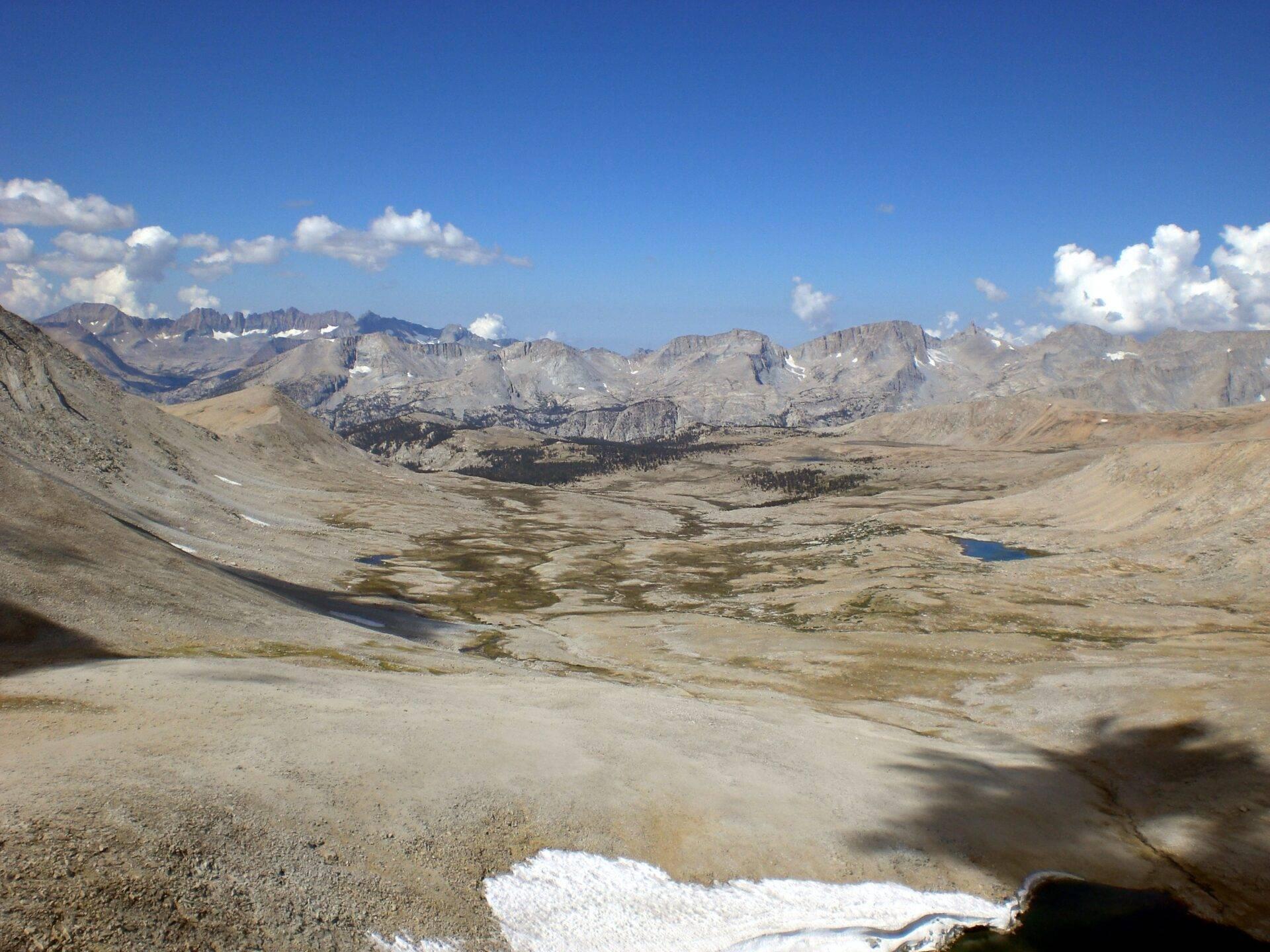 Vista panoramica di una valle alpina desertica con laghi glaciali, vette rocciose e neve residua