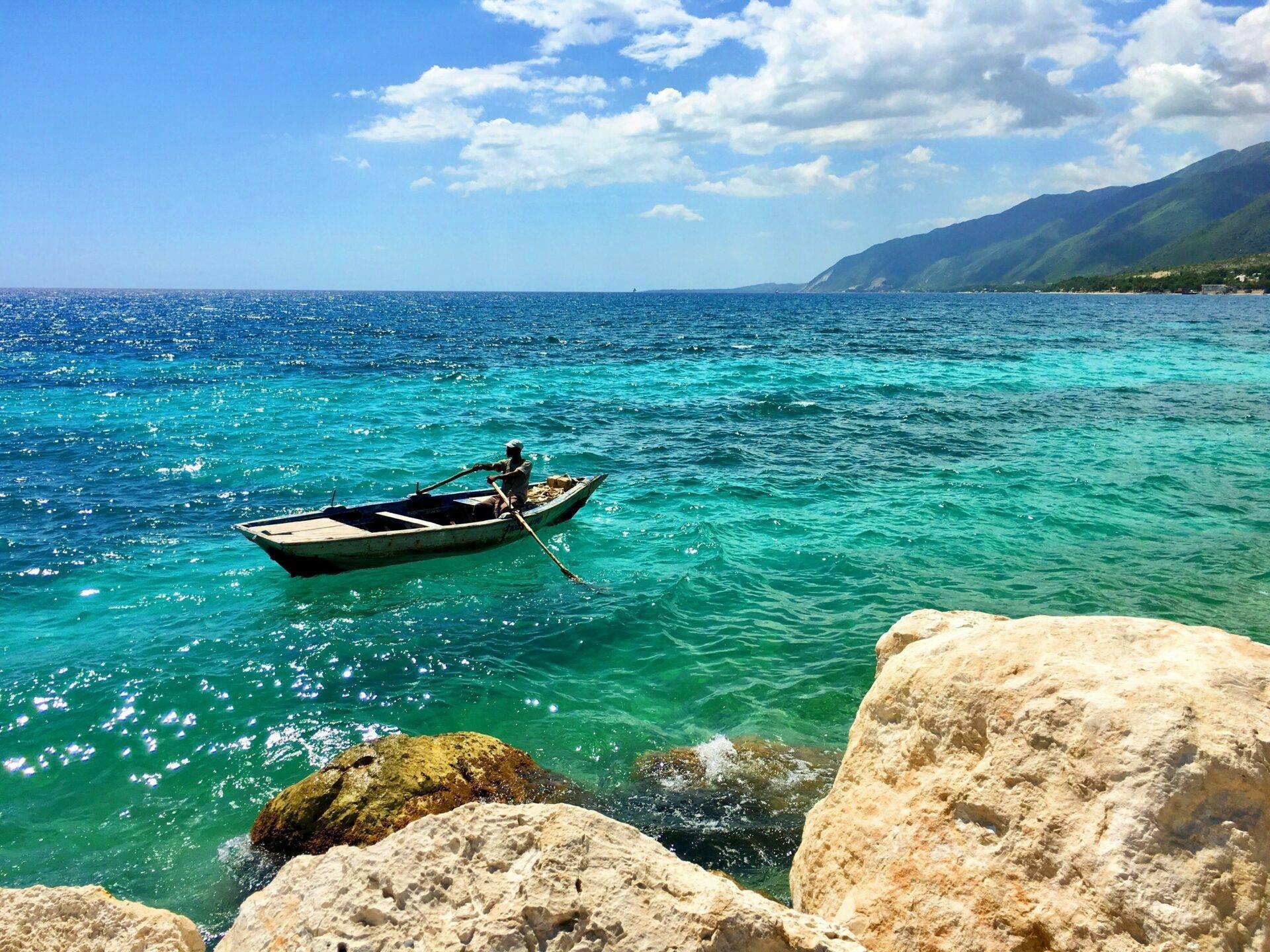 Un pescatore su una barca tradizionale nelle acque turchesi cristalline di fronte a montagne costiere verdeggianti