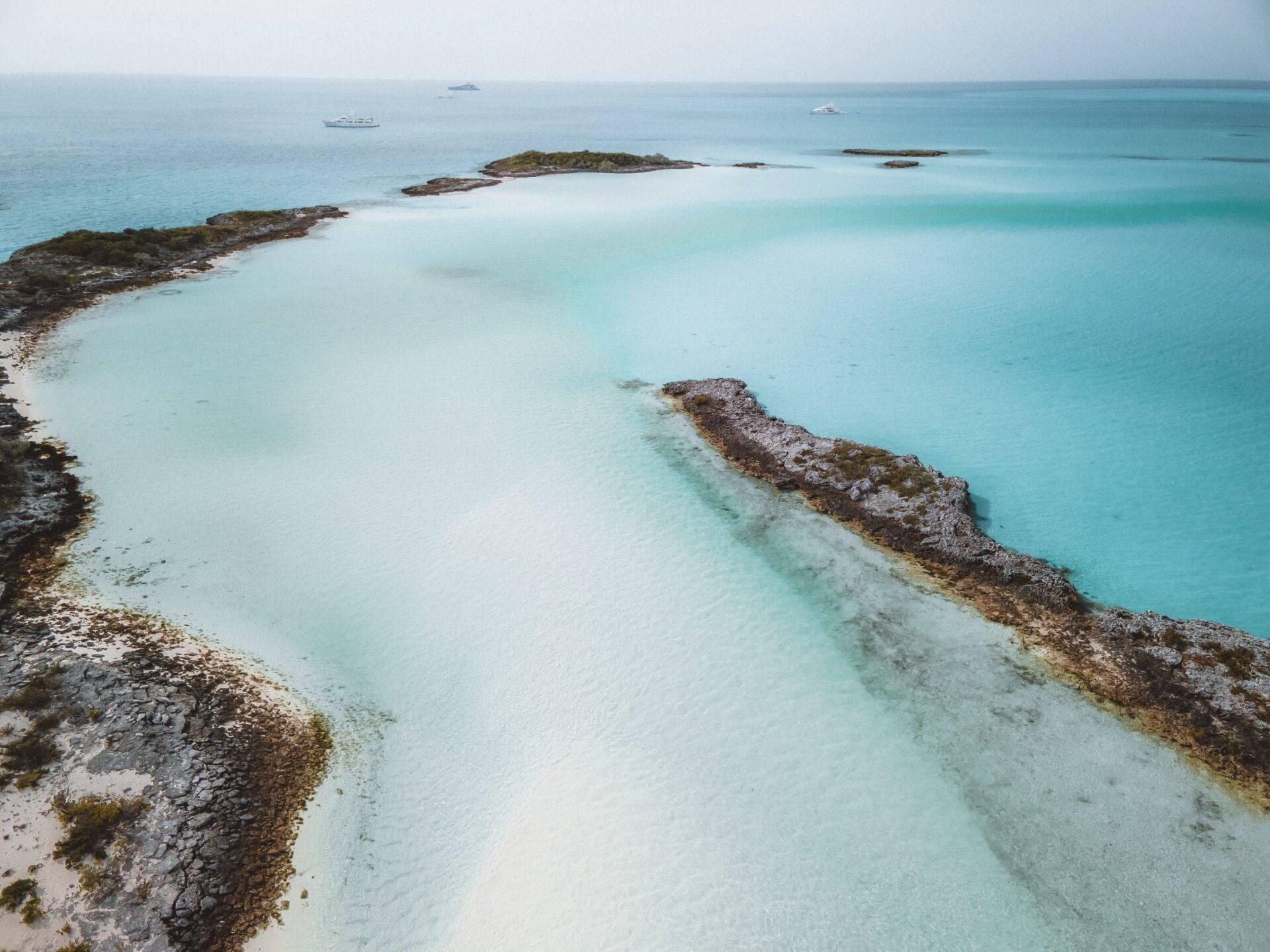 Vista aérea de una laguna turquesa en Bahamas con islotes rocosos y barcos fondeados frente a la costa