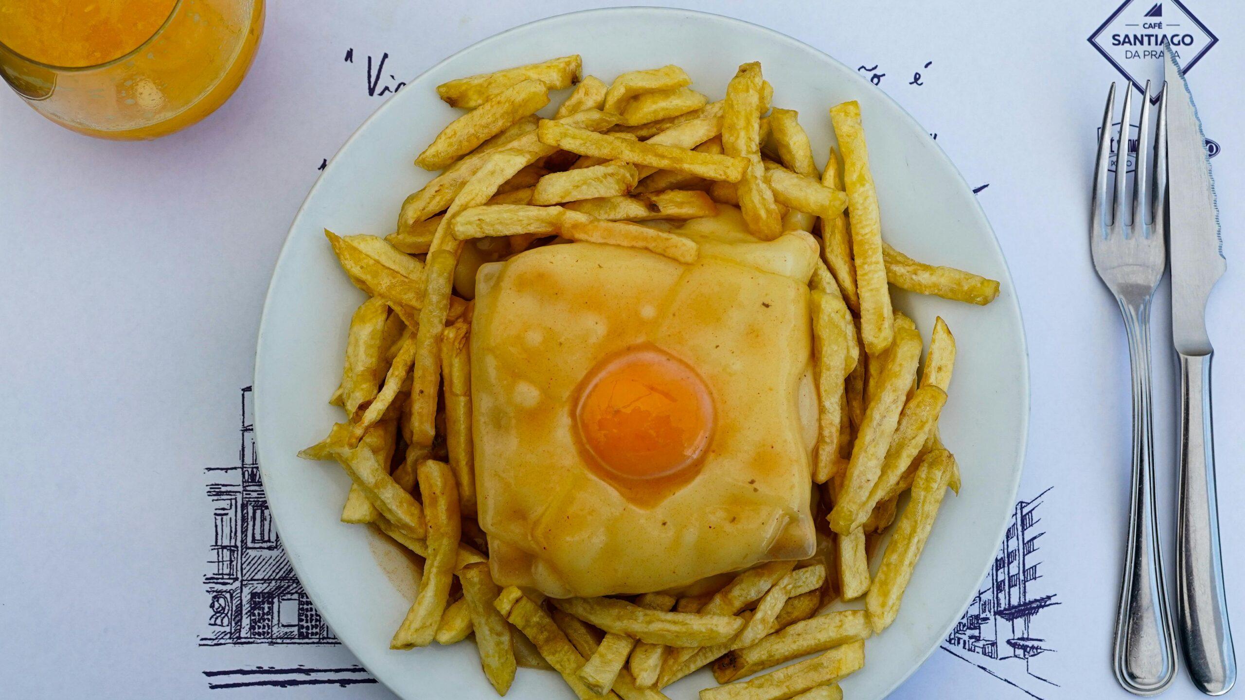 A grilled cheese sandwich topped with a fried egg, surrounded by golden chips, served in a Portuguese restaurant