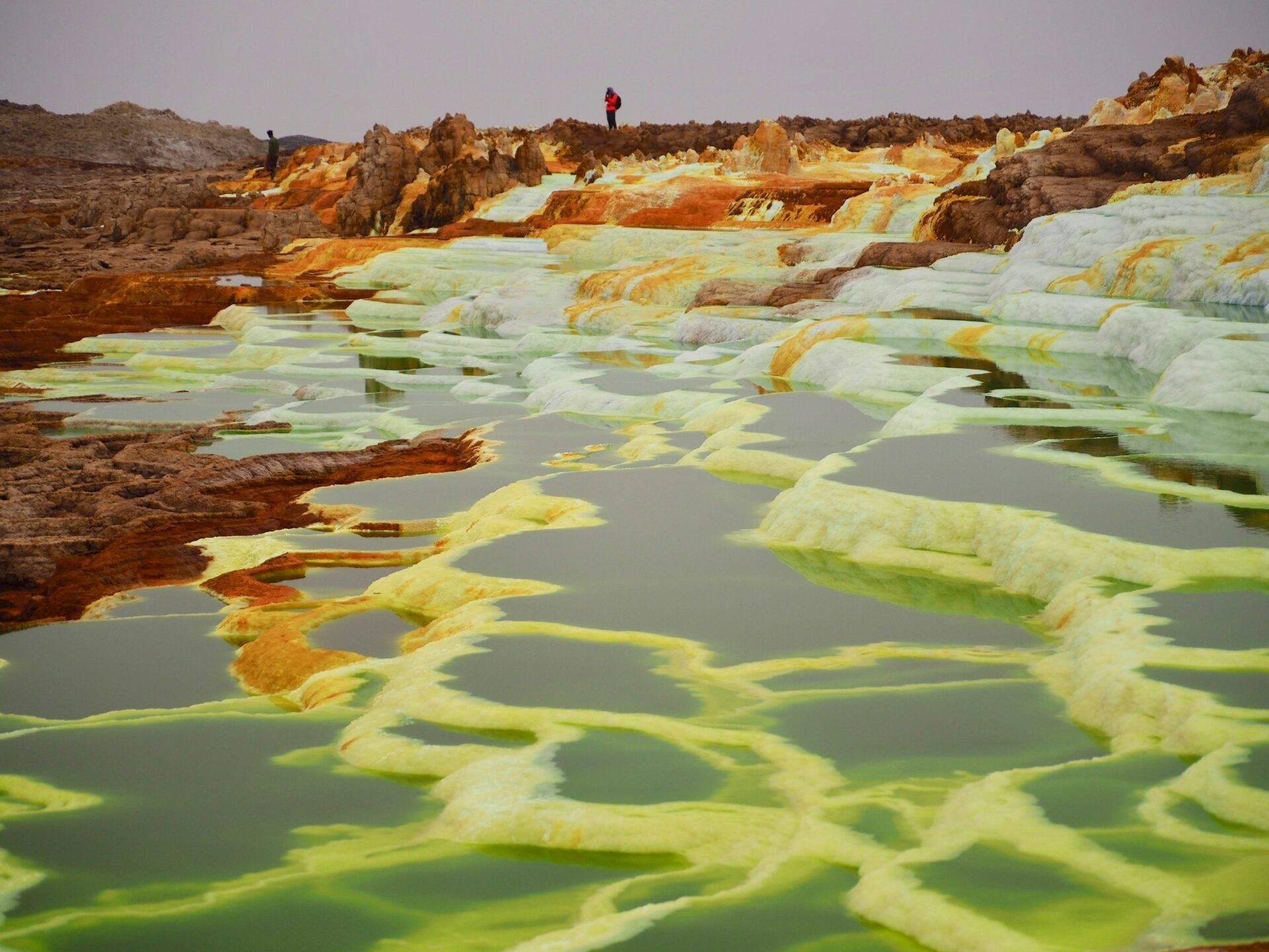Geothermische Becken mit gefärbtem Mineralwasser in Gelb und Grün, mit orangen Fels- und Mineralformationen