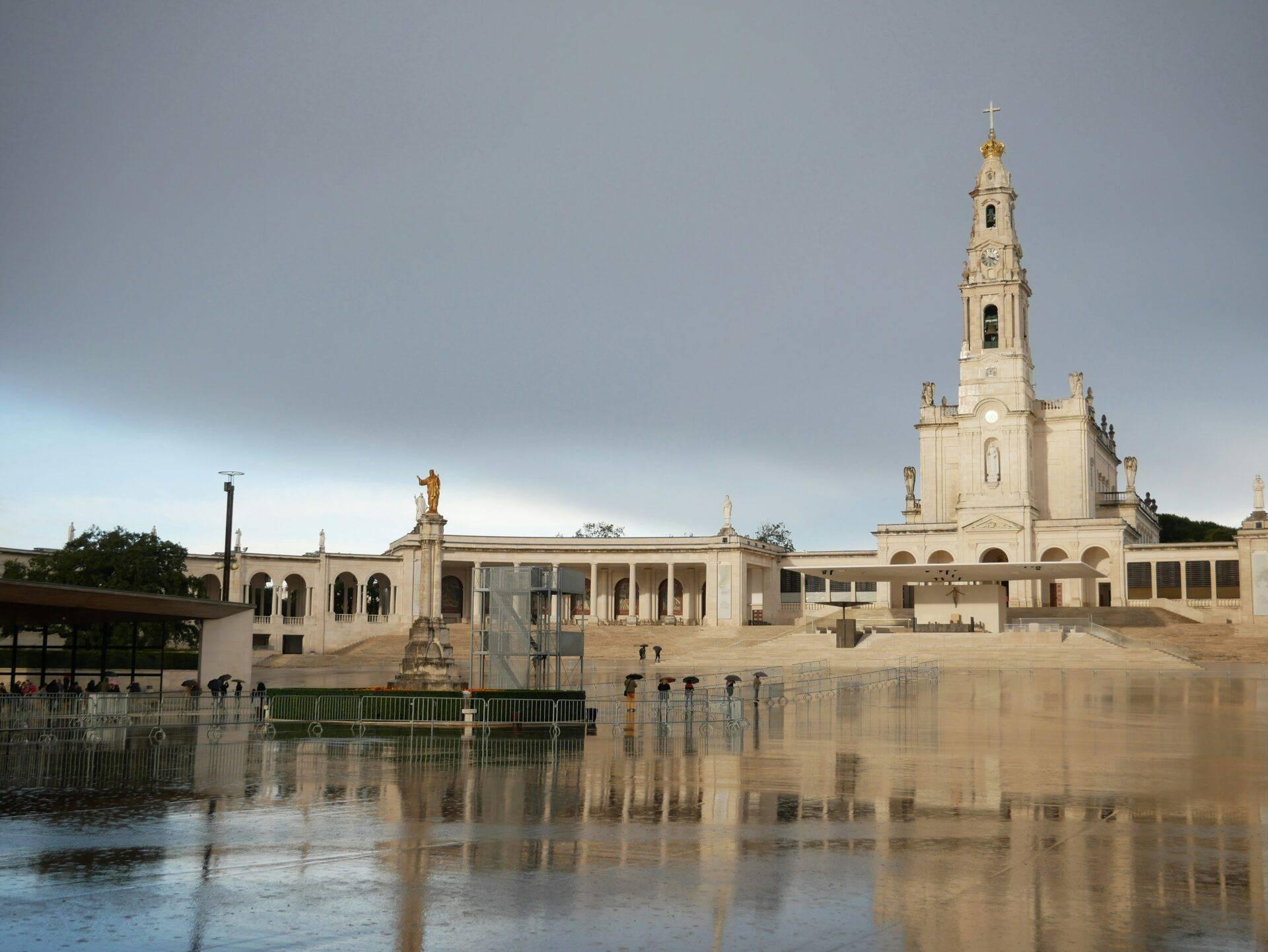 Un santuario religioso bianco con campanile che domina un’esplanade lastricata bordata da acque calme e riflettenti