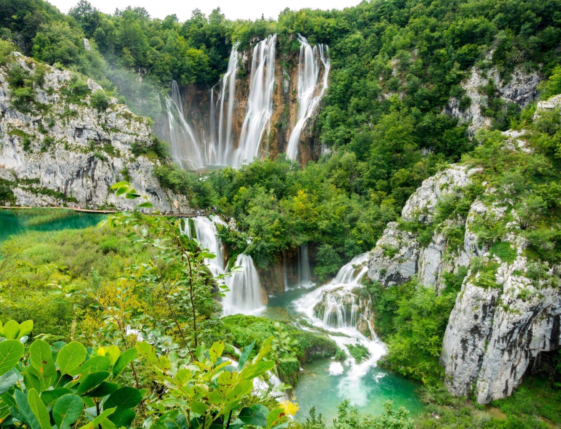 Beeindruckende Wasserfälle stürzen Kalksteinfelsen in einer bewaldeten Schlucht hinab, darunter türkisblaue Seen