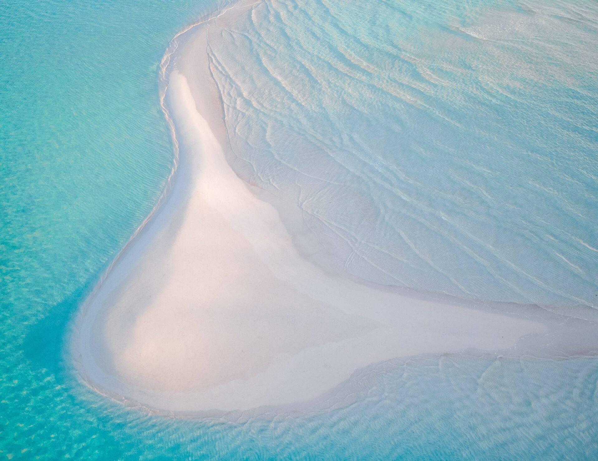 Vista aérea de un banco de arena blanca en forma de media luna rodeado de aguas turquesas poco profundas