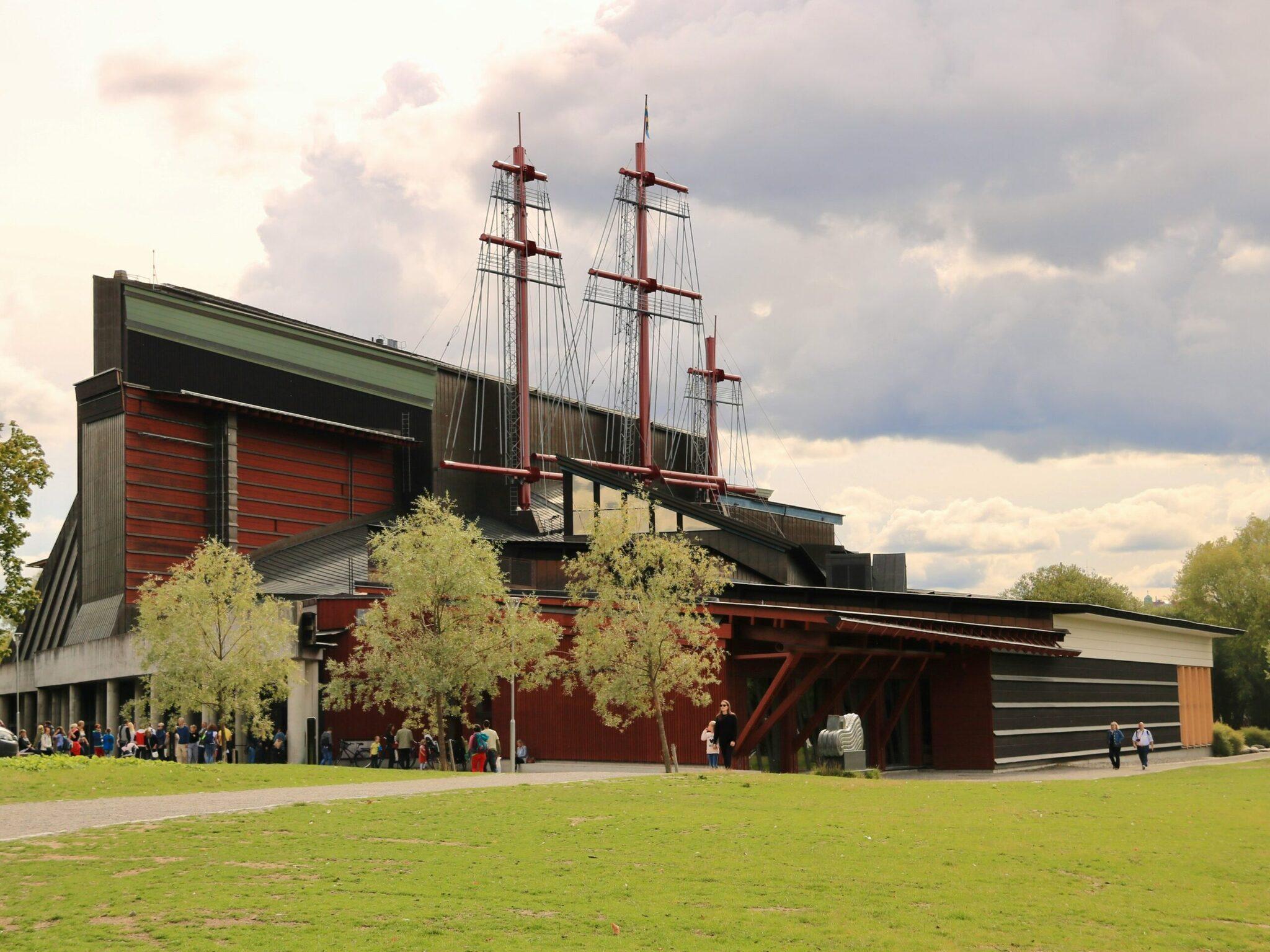 Un moderno museo dalle facciate rosse con una replica di veliero integrata nel tetto, circondato da prati e alberi