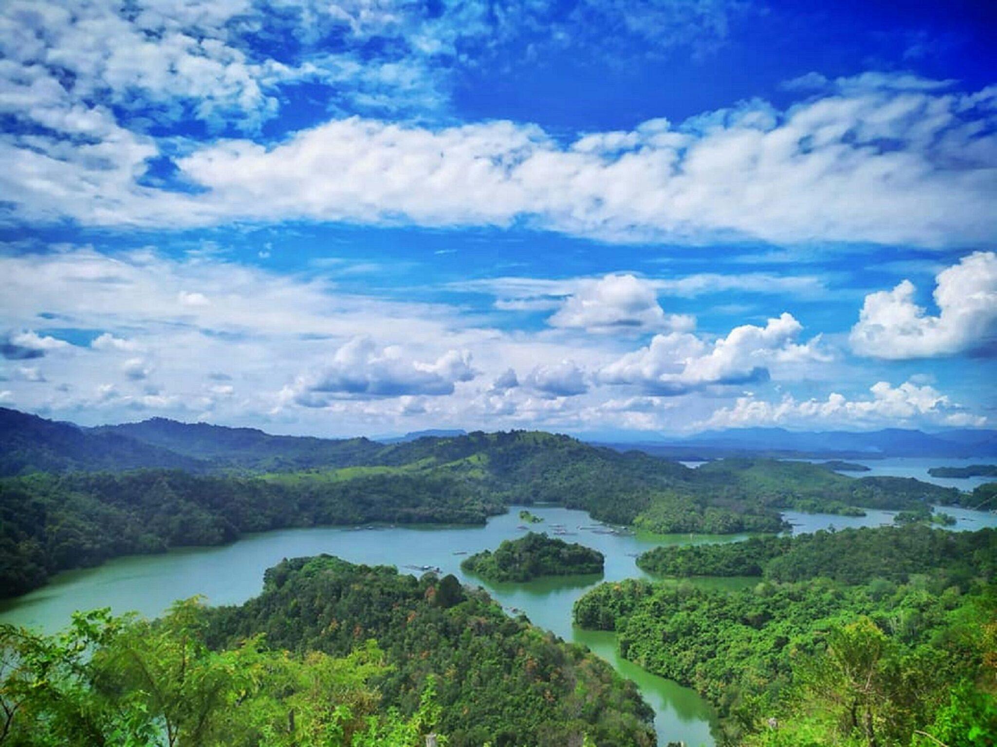 Vue panoramique d’une vallée tropicale avec lacs et forêt dense, montagnes verdoyantes sous ciel bleu nuageux