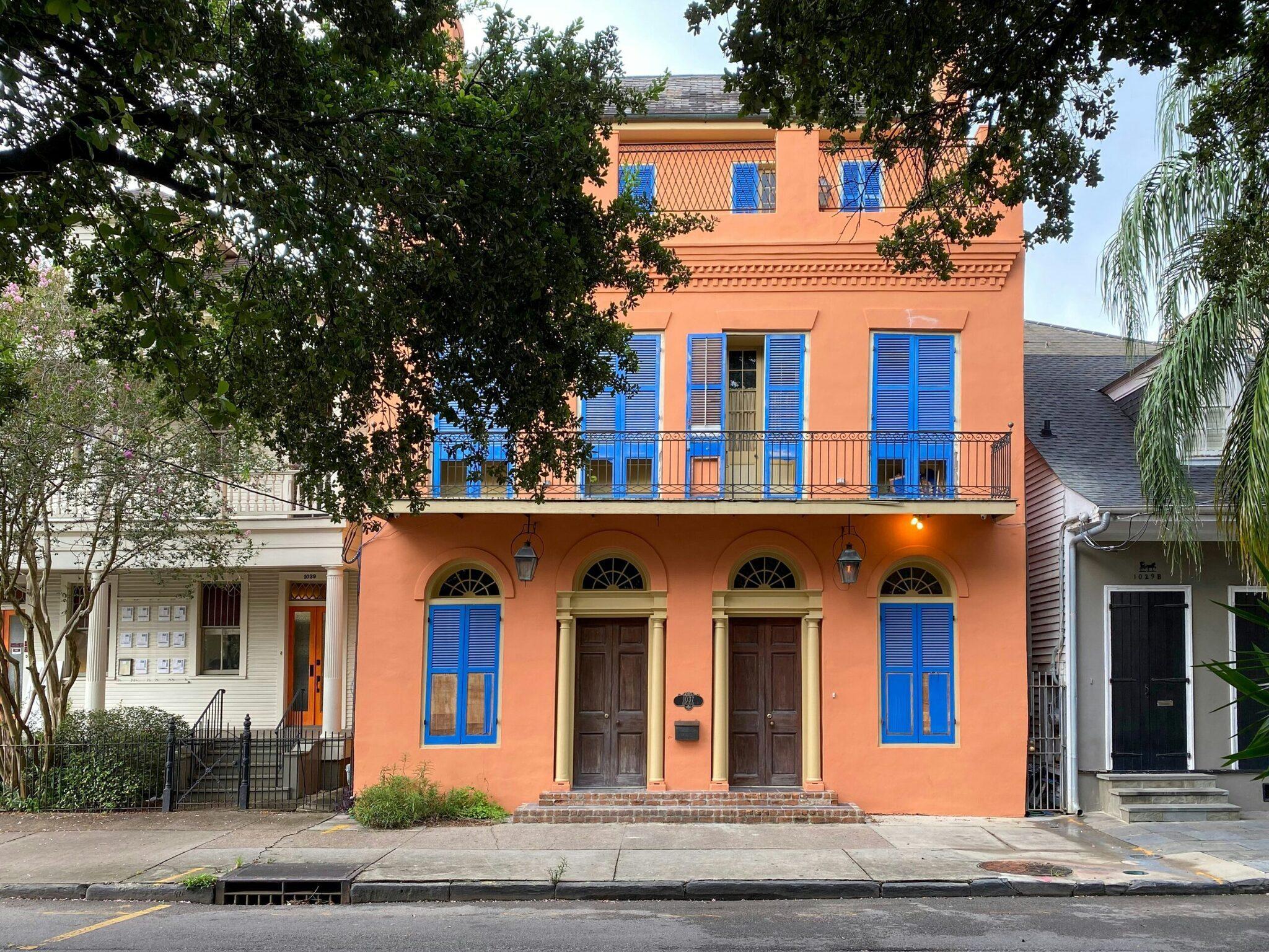 Façade colorée orange et bleu d’une maison coloniale historique bordée d’arbres dans une rue résidentielle