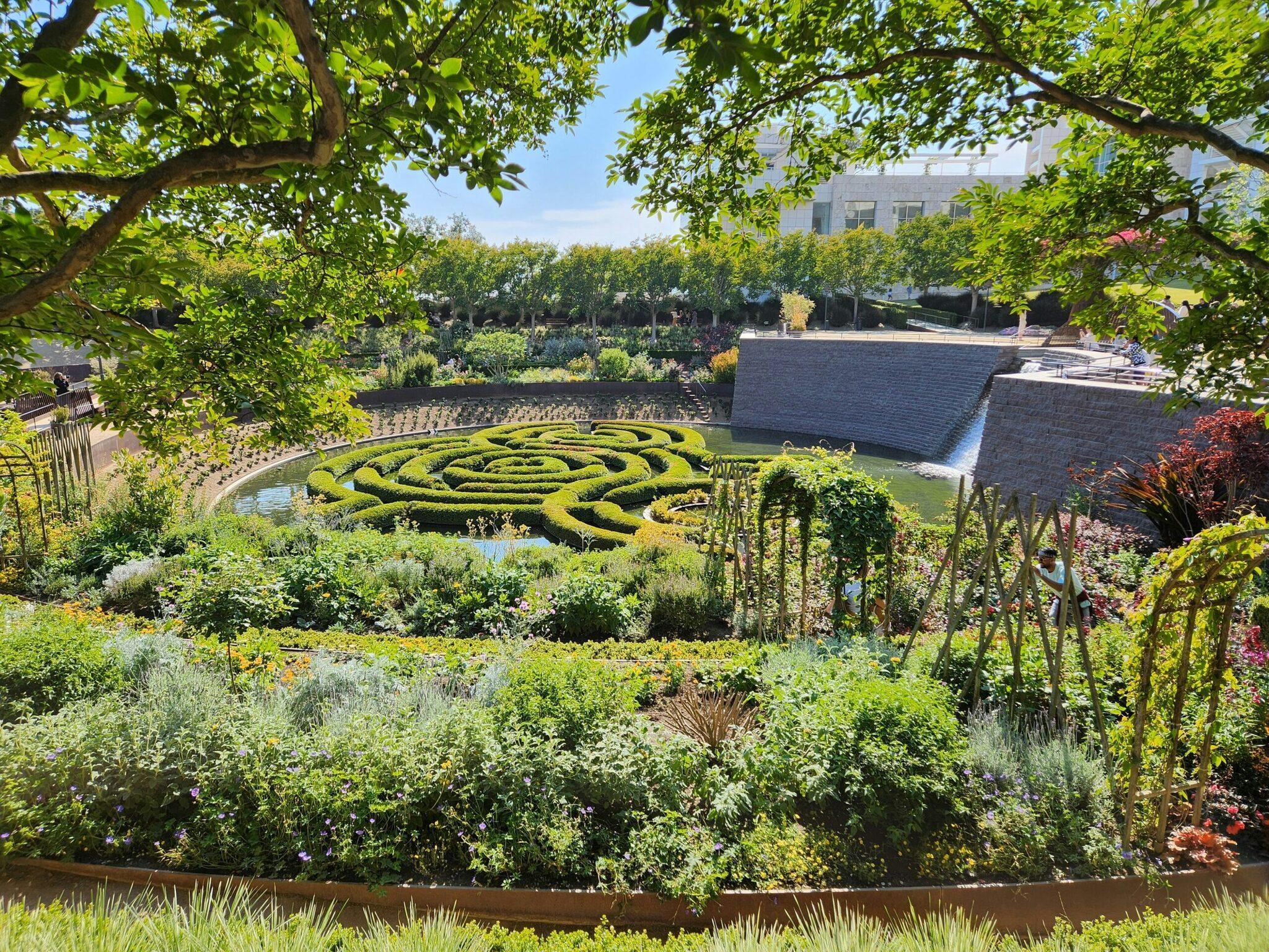 Ein formal gestalteter Garten mit spiralförmigem Buchsbaumparterre, Wasserbecken und einem Steingebäude im Hintergrund