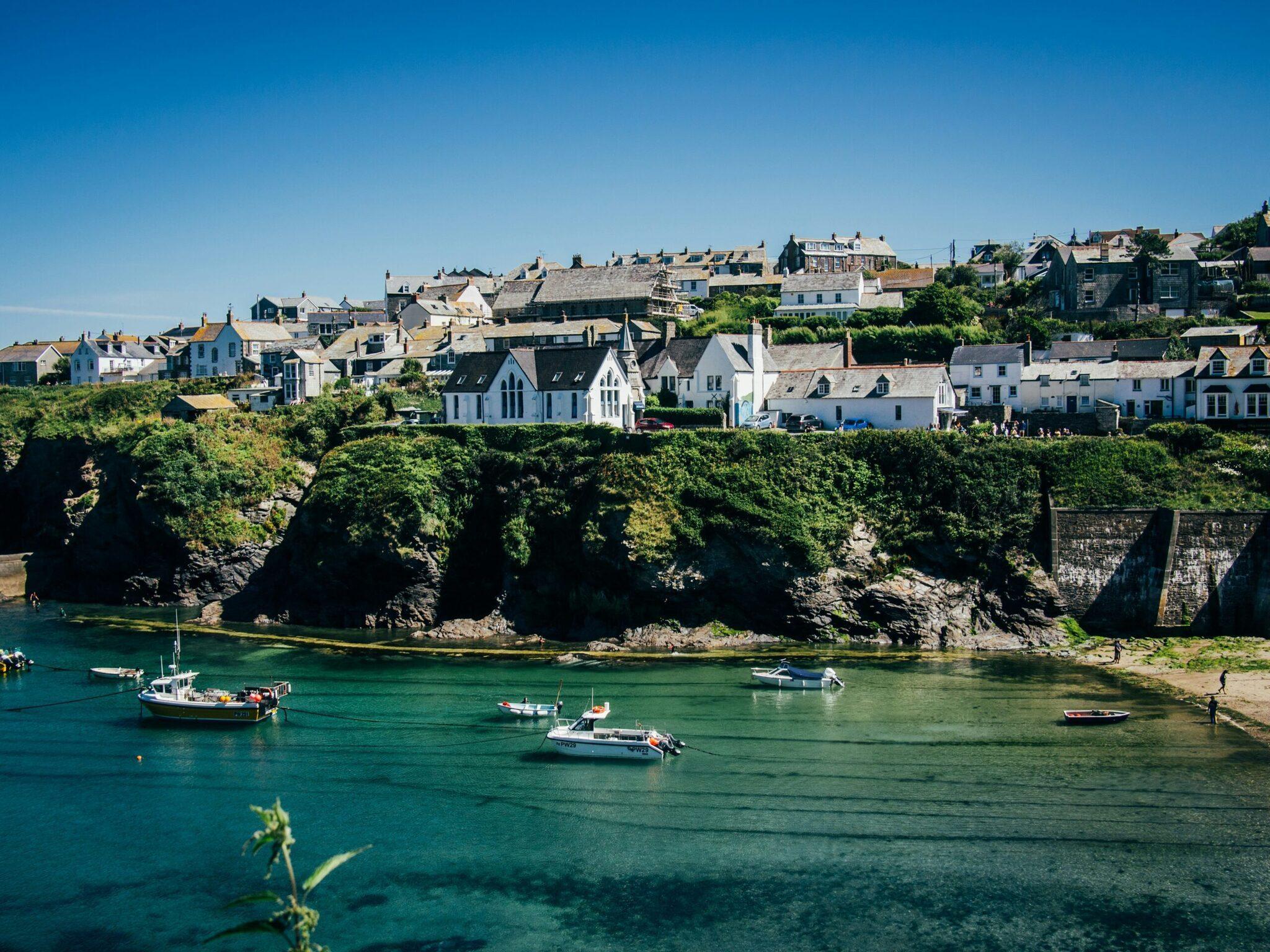 Un petit village côtier avec maisons colorées surplombant un port aux eaux turquoise et bateaux de pêche amarrés
