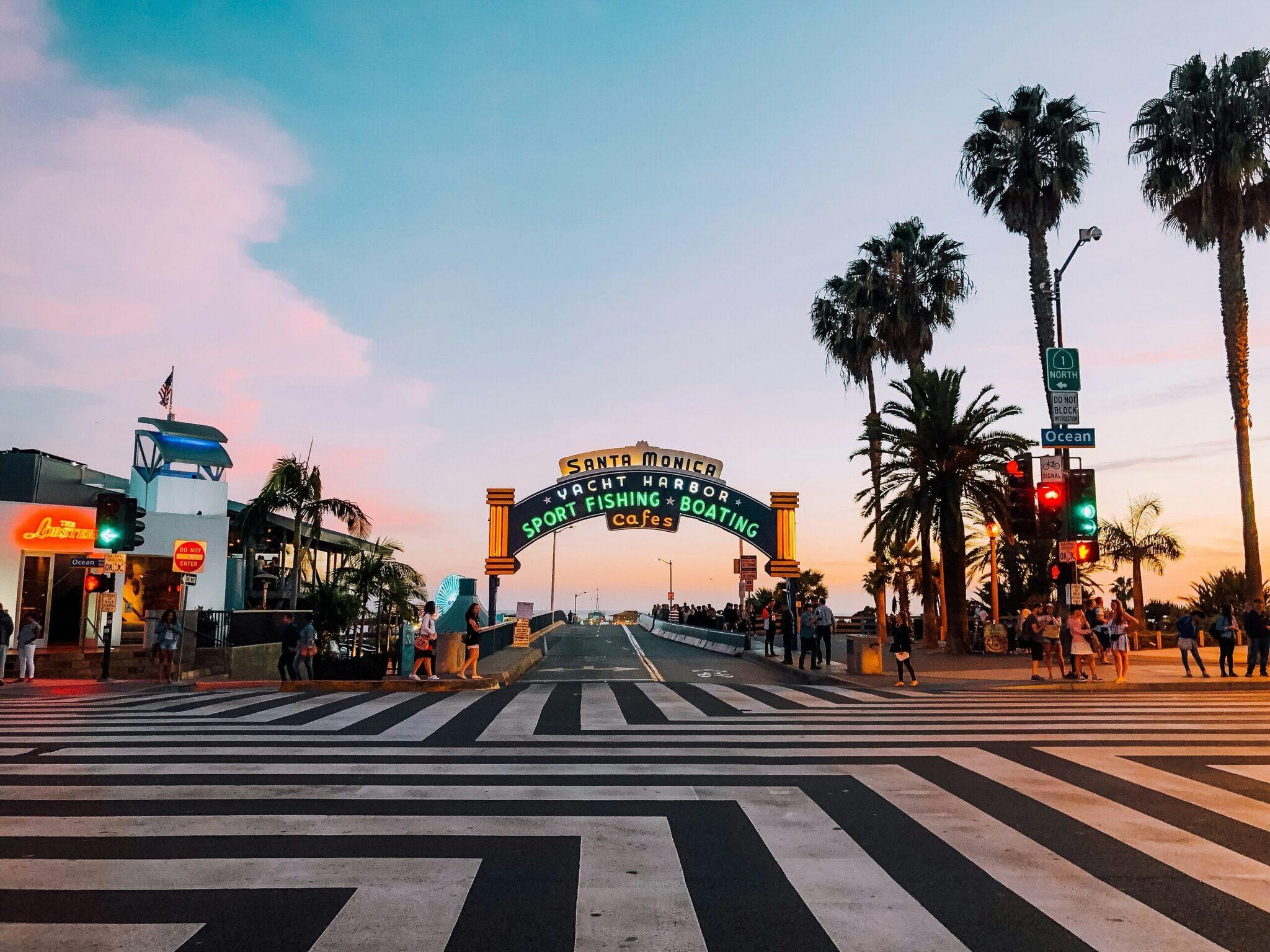 Der ikonische Bogen des Santa Monica Yacht Harbor im Abendlicht, mit Palmen und Fußgängerweg